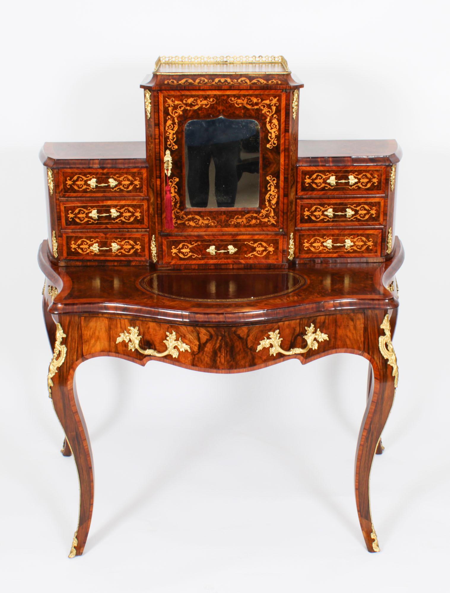 This is a elegant Victorian burr walnut and marquetry Bonheur Du Jour, or Ladies writing desk, circa 1860 in date. 

The superstructure comprises a large central bay with a mirror inset door and a three quarter brass gallery above. The door opens to