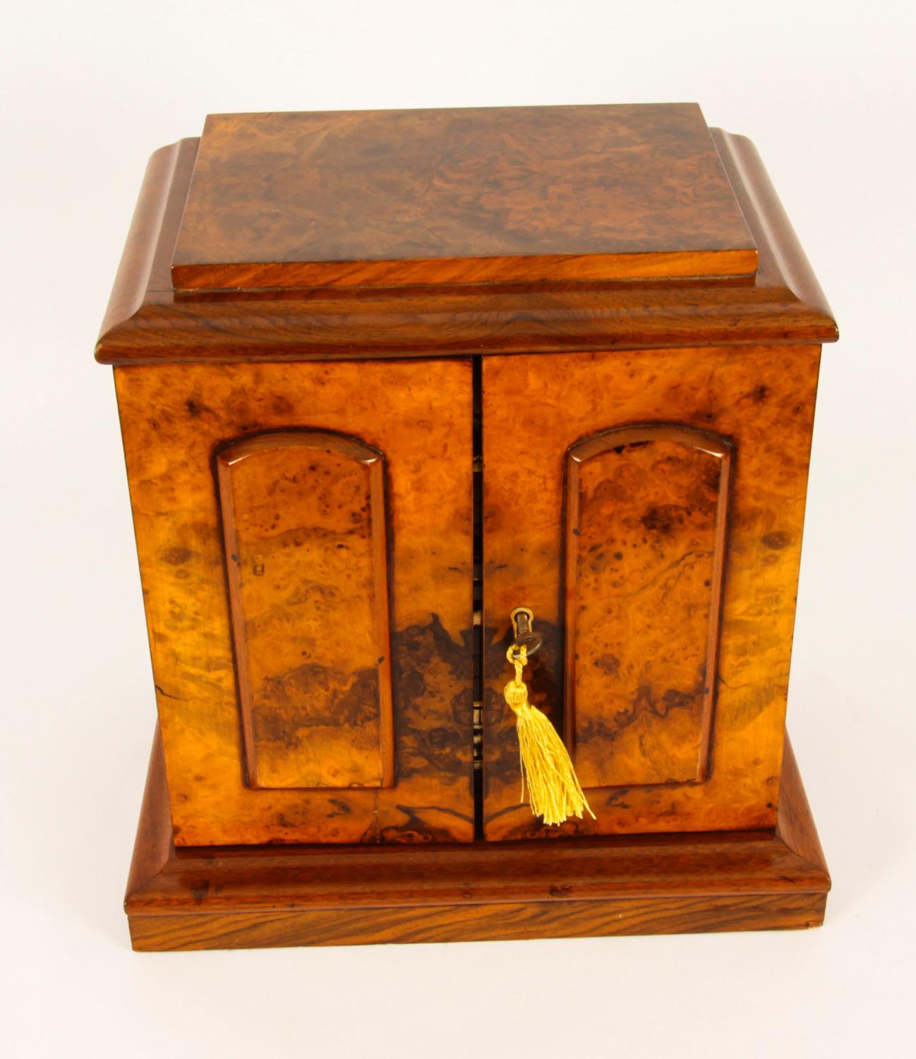 A Victorian burr walnut table cabinet, slightly oversailing pagoda top above a pair of rectangular doors applied with raised arched panels, enclosing three drawers, plinth base, 33cm high, 32cm wide, c.1880

This is a elegant Victorian burr walnut