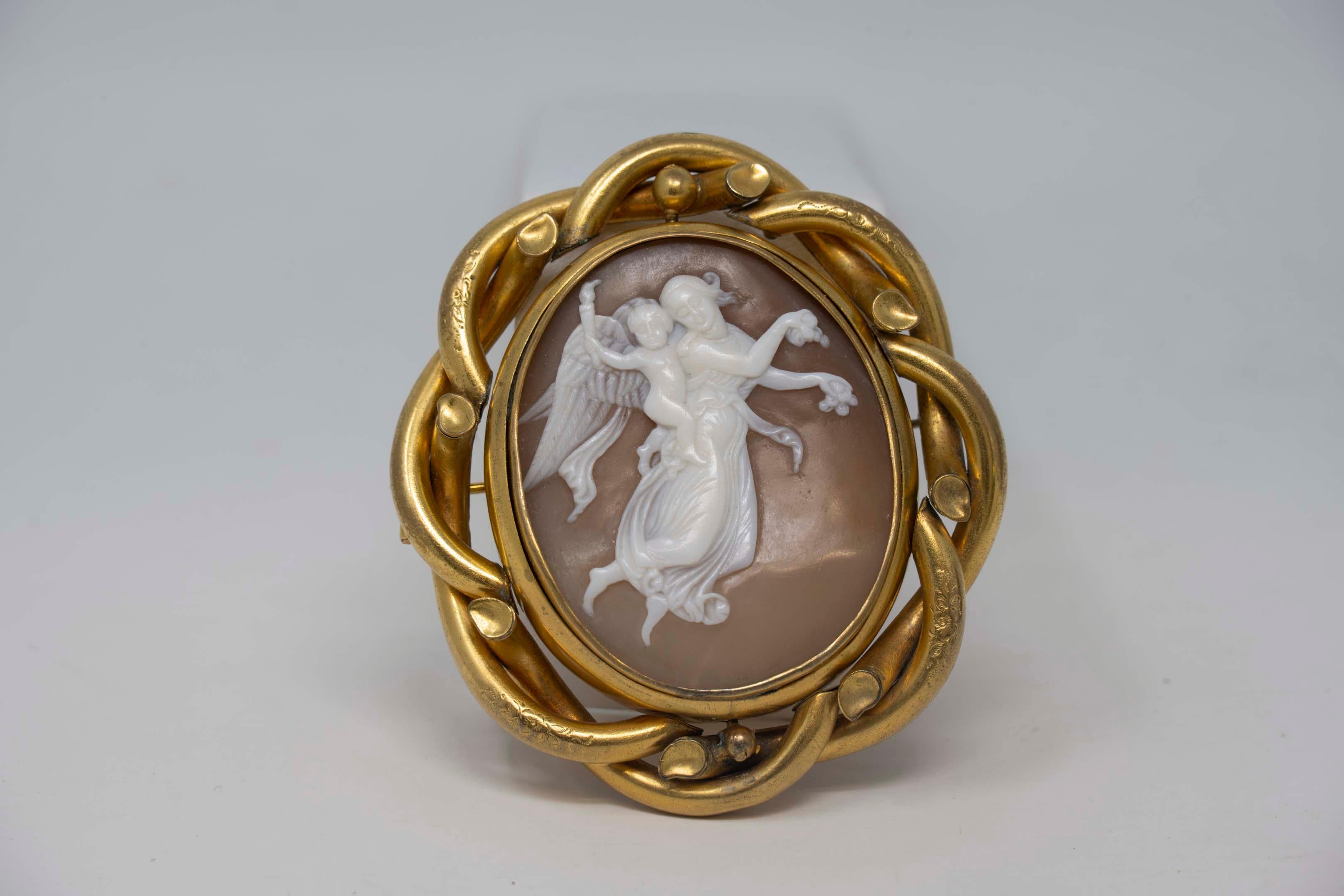 Broche pendentif victorienne en plaqué or représentant Vénus et Cupidon en deuil. Le tour central, comme le montre la photo au dos, est scellé avec du cristal, aucune marque trouvée, vers 1880. En bon état, la broche mesure 7,2 cm x 6,5 cm. Le camée