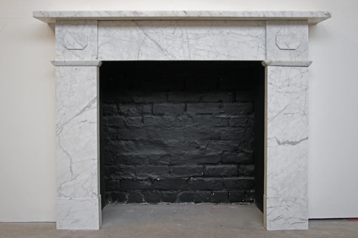 Antique Victorian Cararra marble fireplace surround. Square boxed section capital with applied octagonal lozenge above stepped interruption, plain jambs and boxed section plinths. Circa 1880.

For detailed sizes please see the size diagram in the