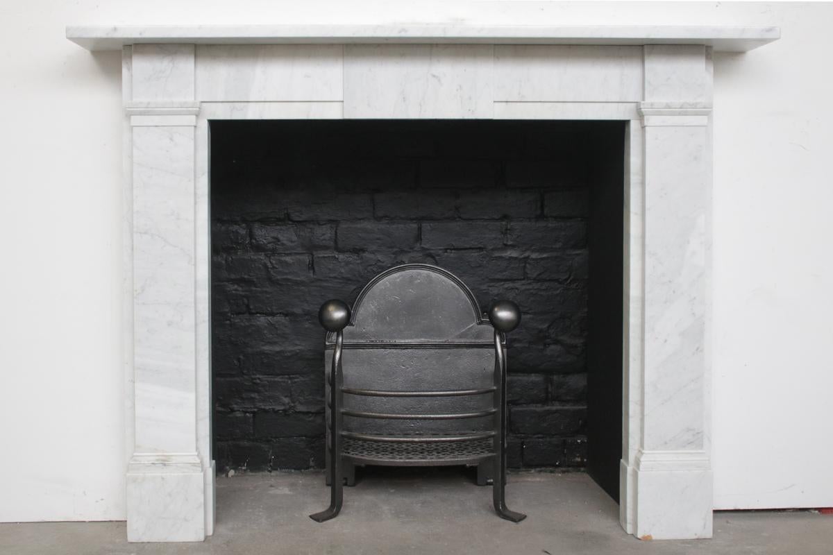 An antique Victorian Carrara marble fireplace surround good proportions and simple form. With plain capitals flanking the stepped frieze centred with a plain tablet. Circa 1850.

Pictured with an original fire basket, sold separately.

For