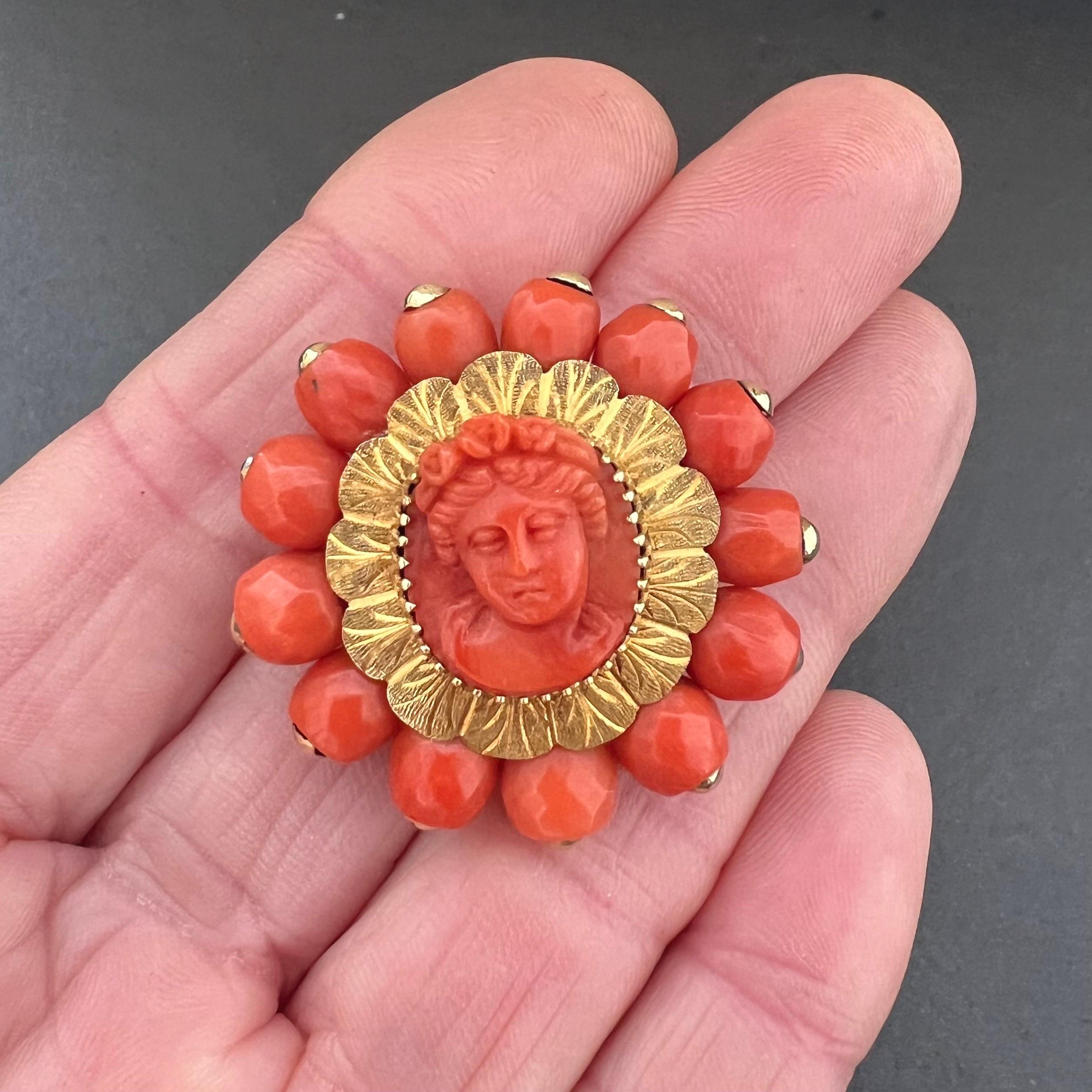 A beautiful 14 karat yellow gold hand-carved in high relief coral brooch set with a cameo in the center. The large coral beads on the edge are faceted and have a gold cap at the top and attached to the brooch. The beautifully carved oval cameo shows