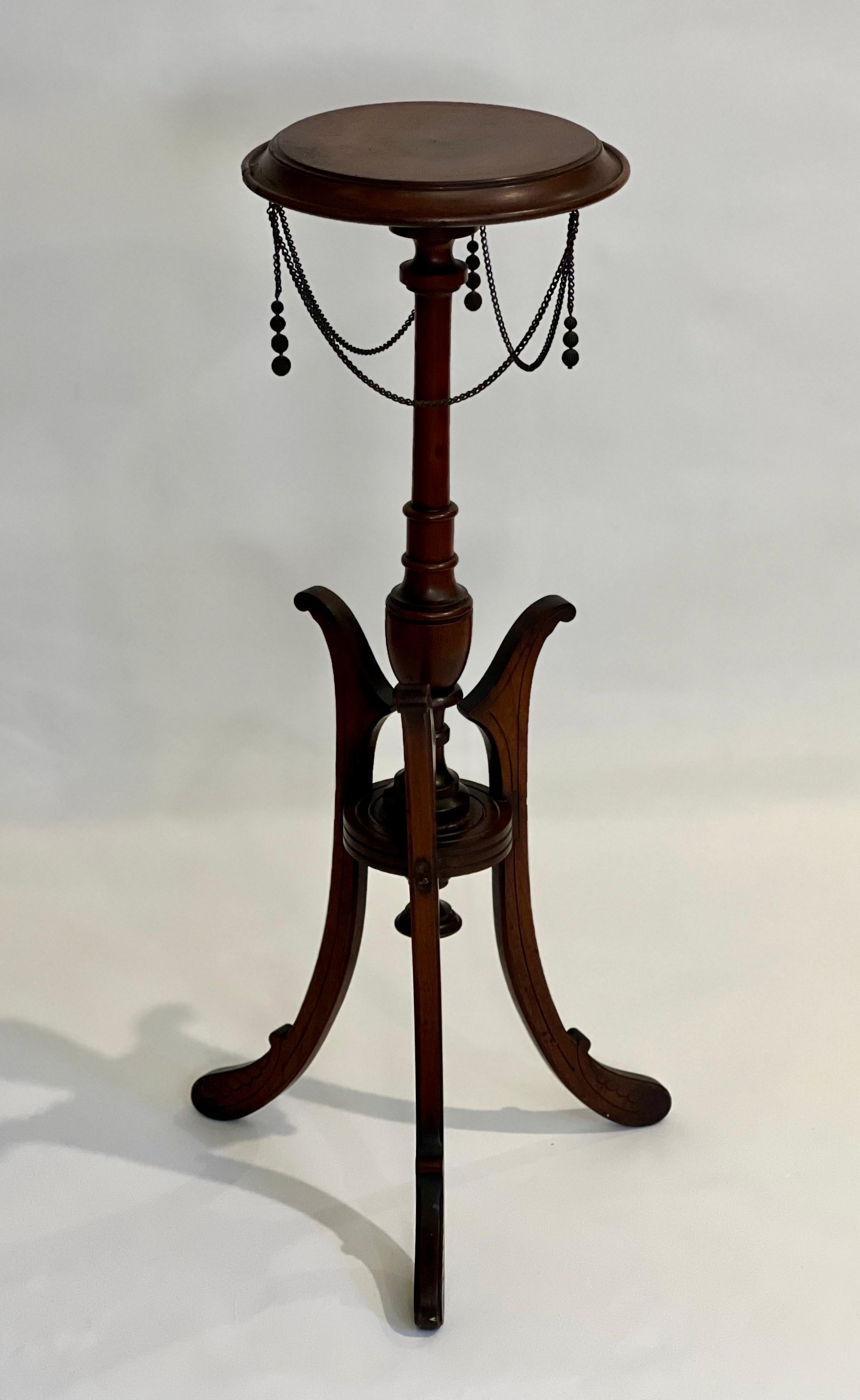 Antique Victorian mahogany pedestal plant stand, c. late 19th century.

Beautifully carved pedestal with a metal chain swag adorning the circular top. The tripod base has an incised design defining the curvature of the legs down to the rounded feet.