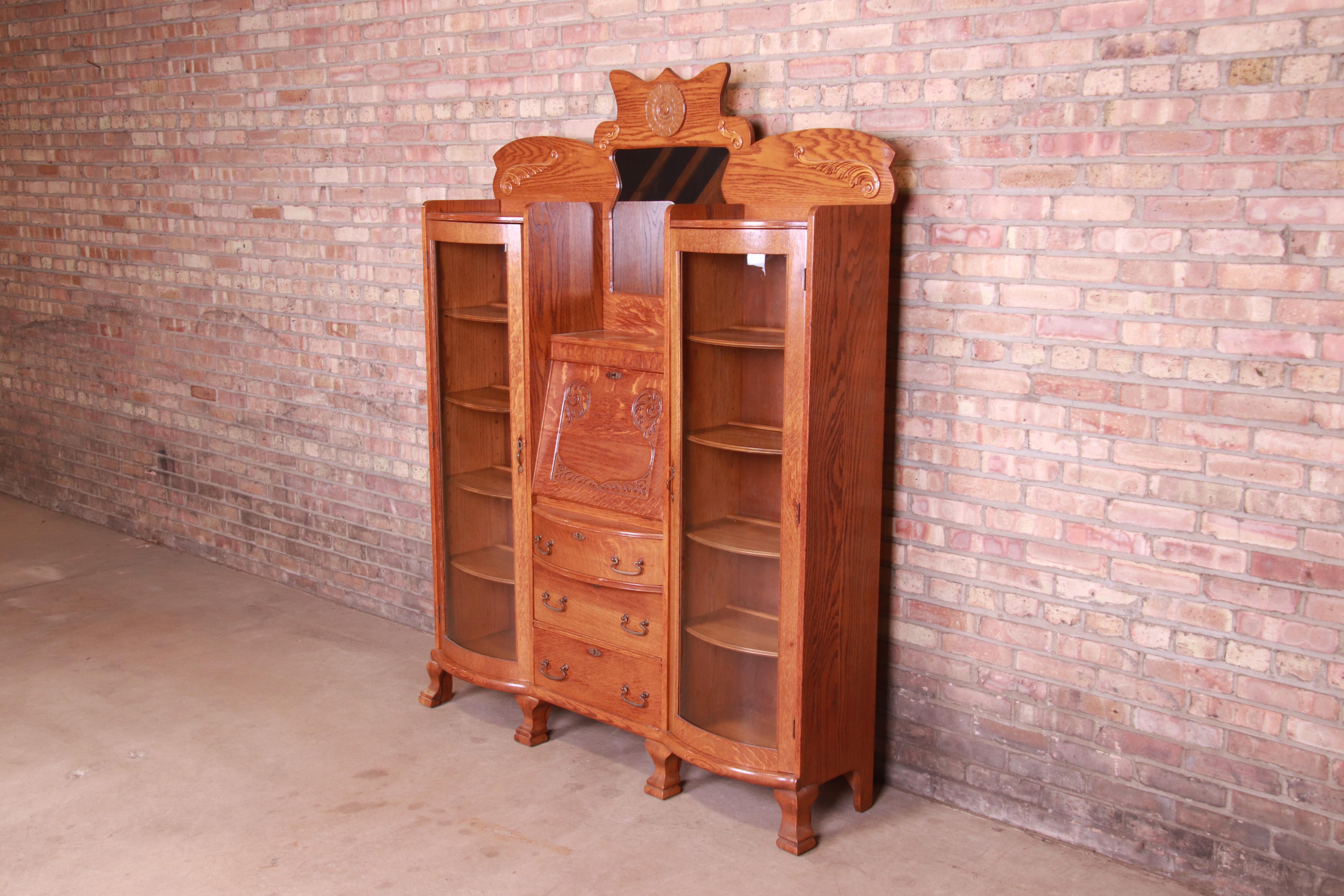 A gorgeous antique Victorian double bookcase wall unit with drop down secretary desk and mirror

USA, Circa 1890s

Carved solid oak, with curved glass doors and original brass hardware. All drawers and doors lock, and original key is