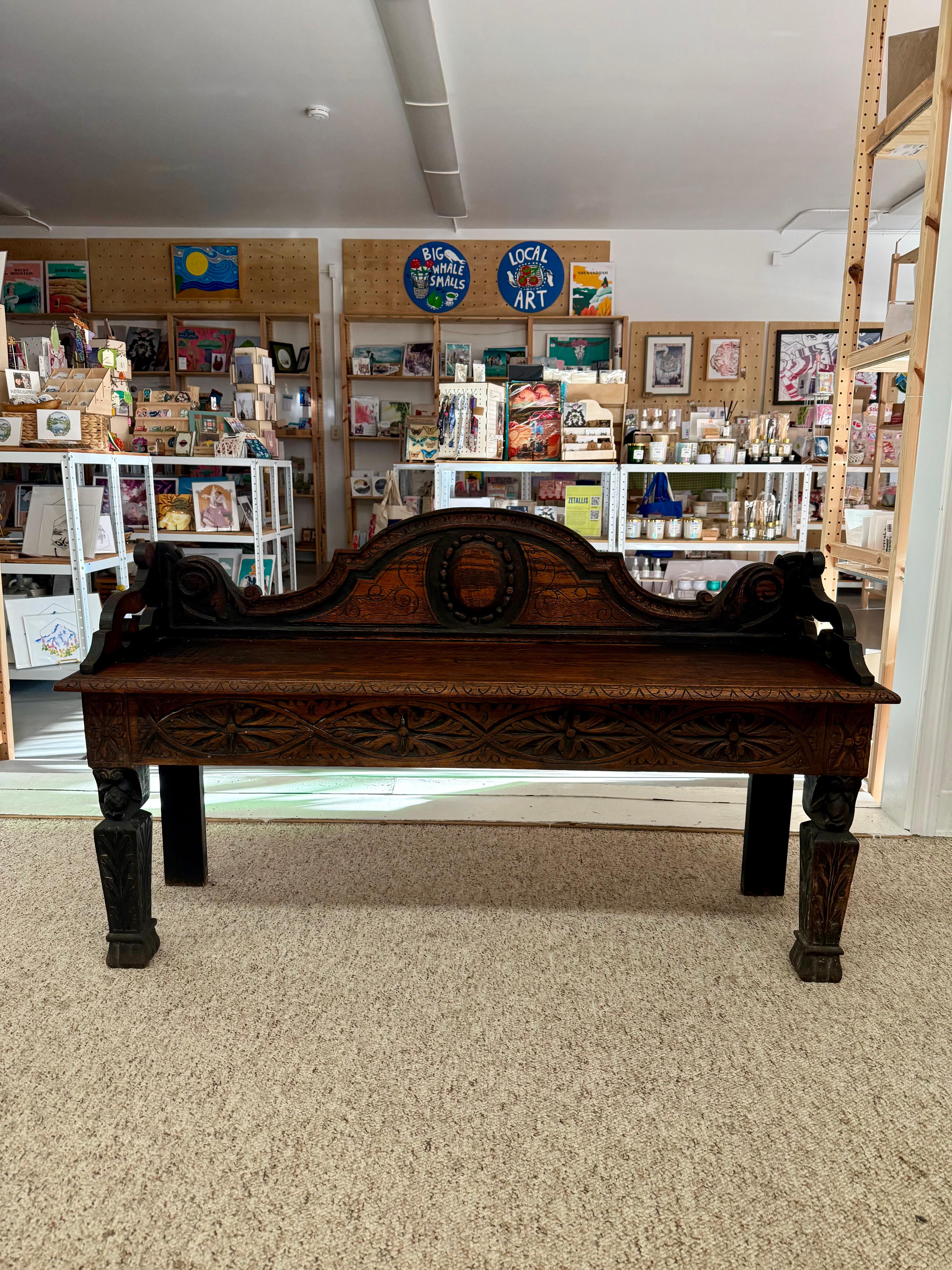  The bench is crafted from dark-stained hardwood, likely oak, with a smooth rectangular seat. It features intricately carved legs with floral and geometric patterns, some with animal or mythical creature heads, and matching carved edges. The sides