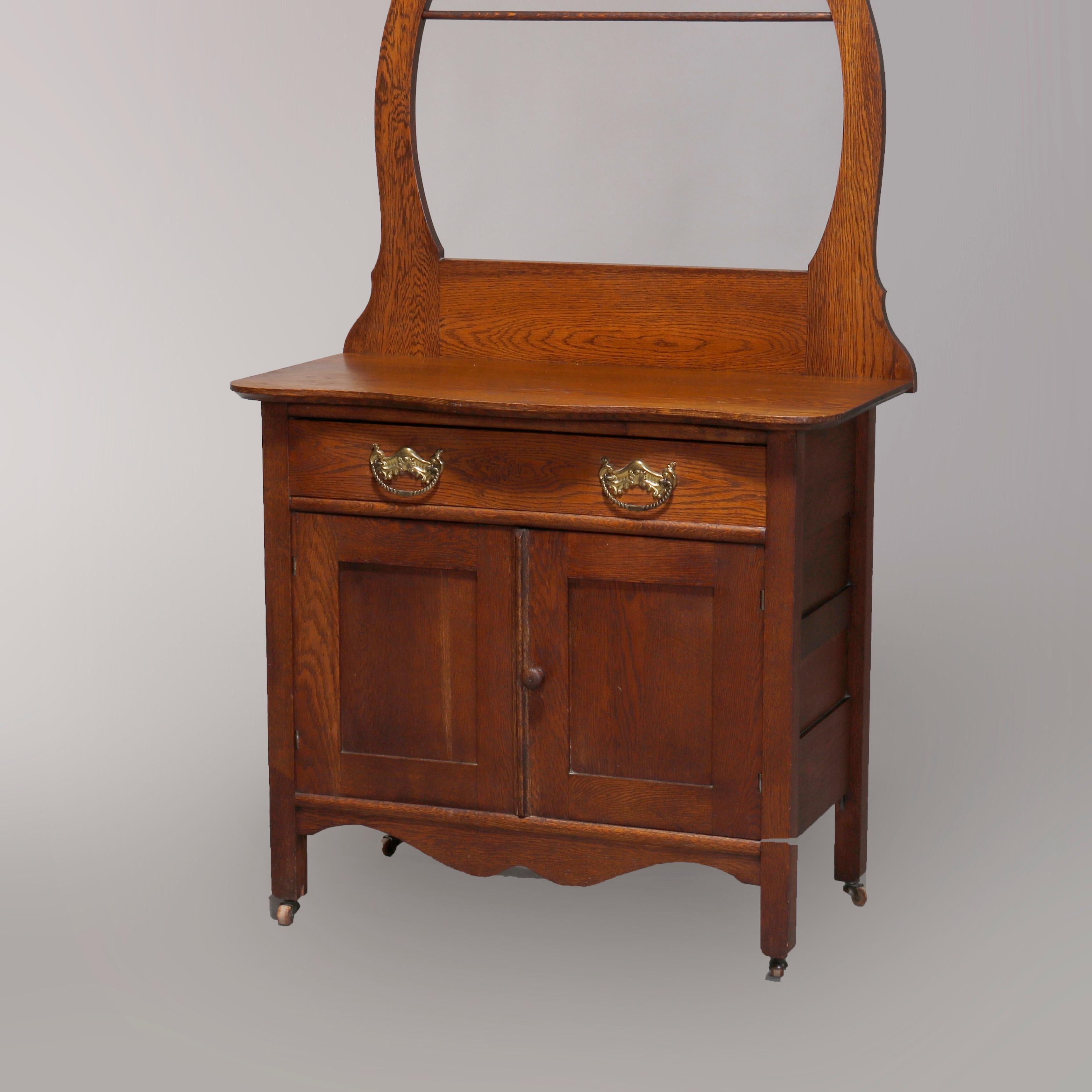 An antique Victorian Hotel Commode by Muncy Mfg. offers oak construction with upper mirror having carved scroll crest and surmounting case with linen bar and shaped top over frieze drawer and double door cabinet, en verso original labels as