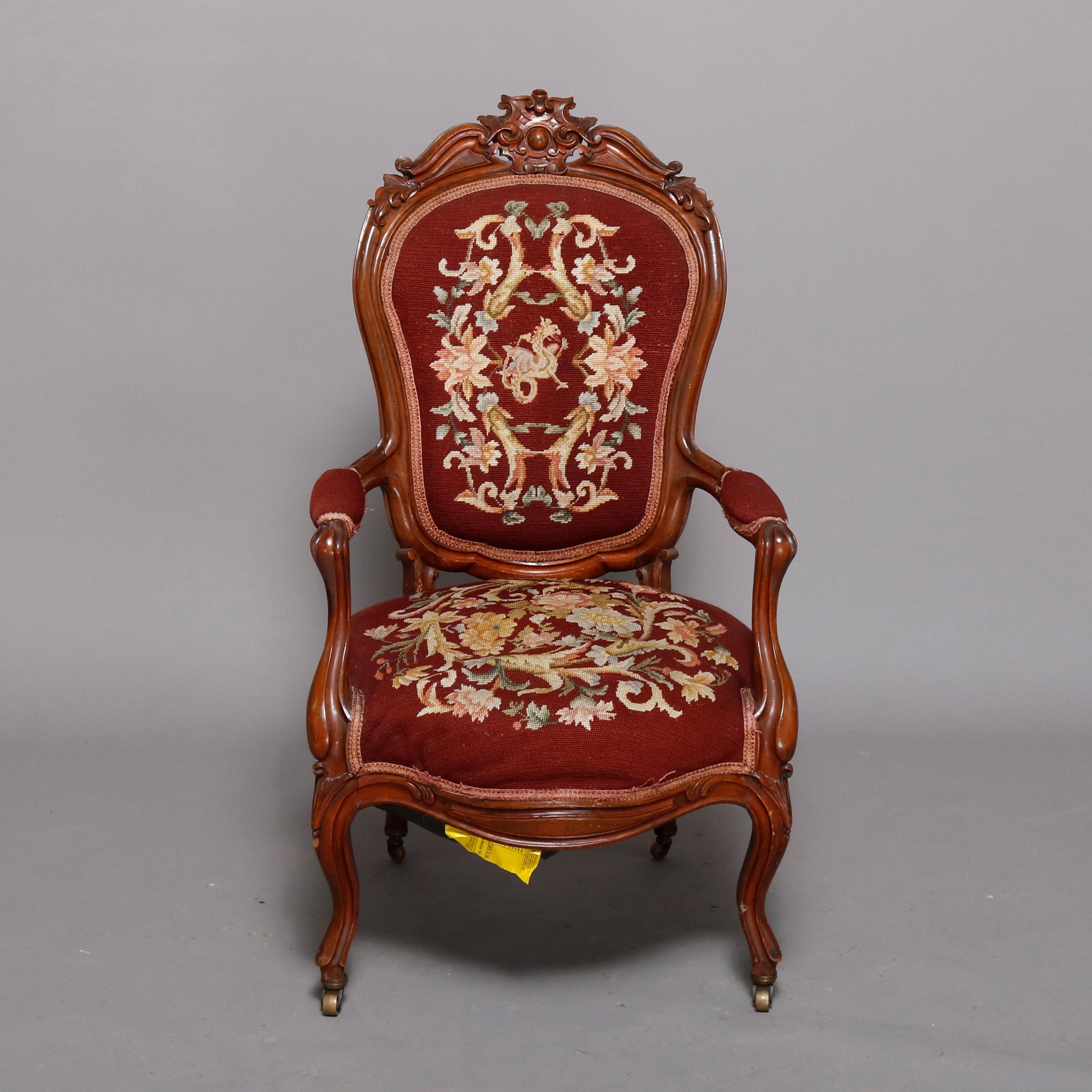 An antique Victorian gentleman's parlor armchair features rosewood frame with deeply carved scroll and foliate crest surmounting shield form back having floral needlepoint upholstery, covered arms and matching seat, raised on cabriole legs, circa
