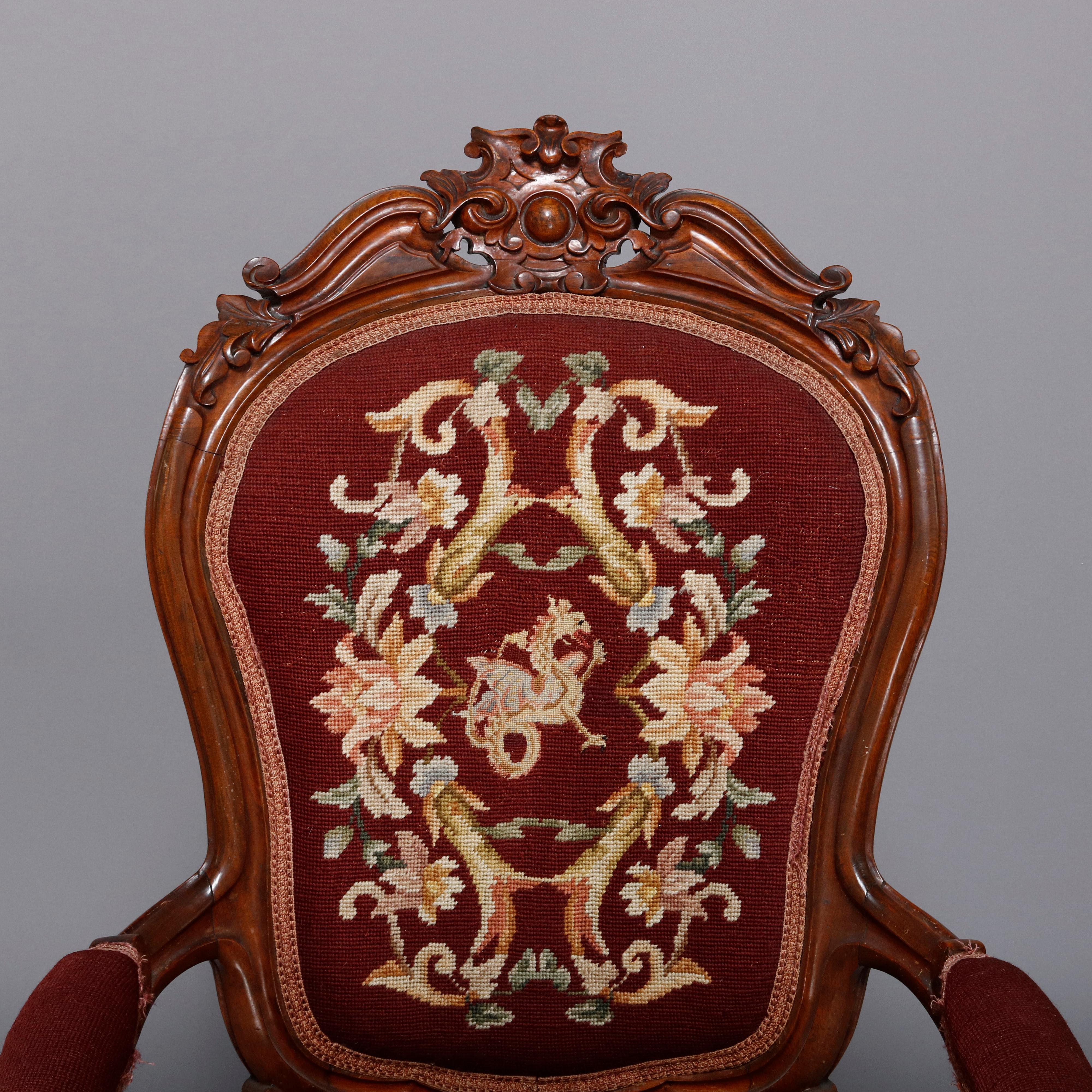 An antique Victorian gentleman's parlor armchair features rosewood frame with deeply carved scroll and foliate crest surmounting shield form back having floral needlepoint upholstery, covered arms and matching seat, raised on cabriole legs, circa
