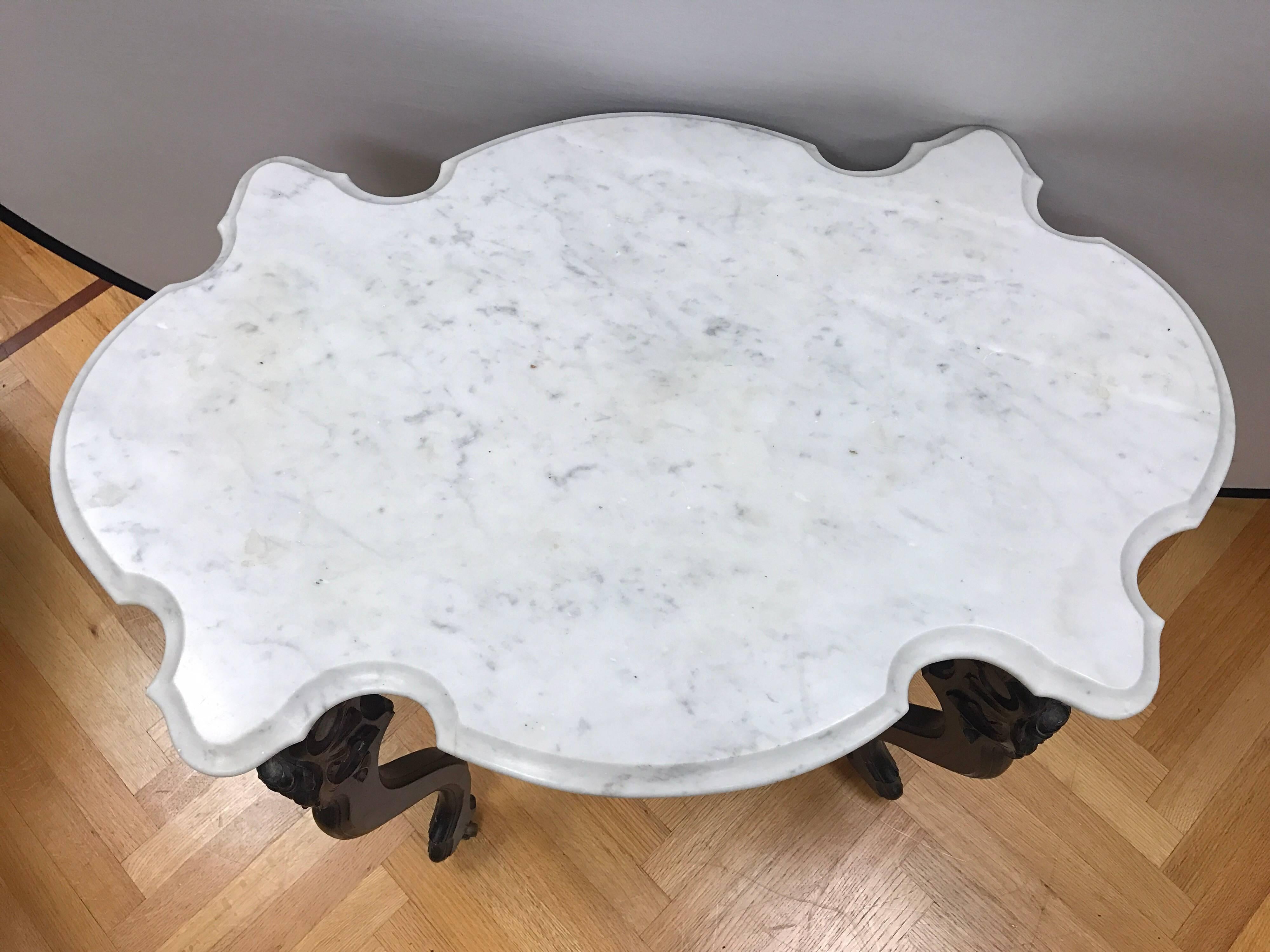 19th century Victorian walnut table with intricate carved detail on base. Top is white marble with grey veining and has a bevelled edge. Has castors for ease of movement.