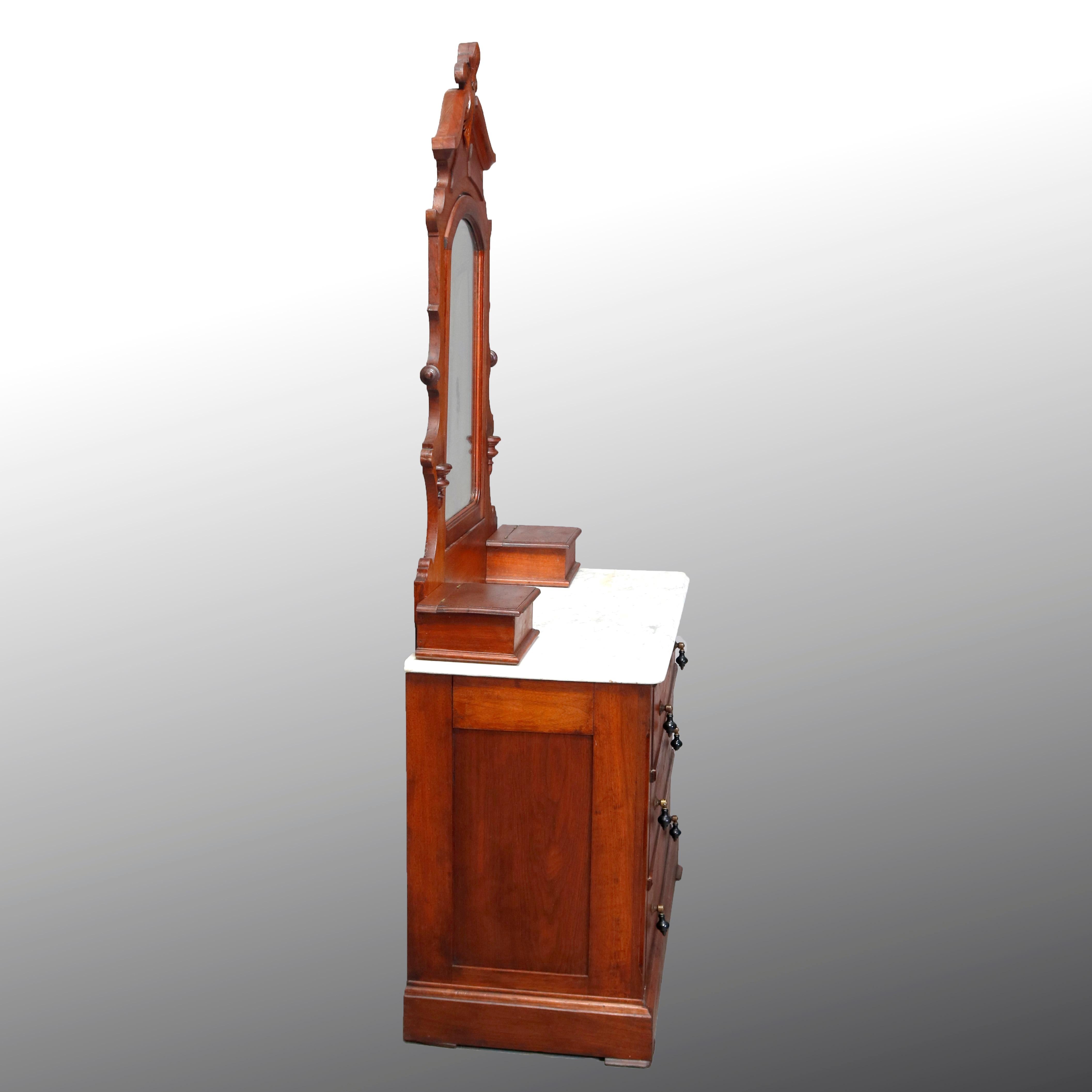 An antique Victorian dresser offers walnut construction with a tall mirror having frame with carved fleur des lis crest surmounting base with flanking lift-top glove boxes on a case with marble top and three long drawers each having tear drop pulls,