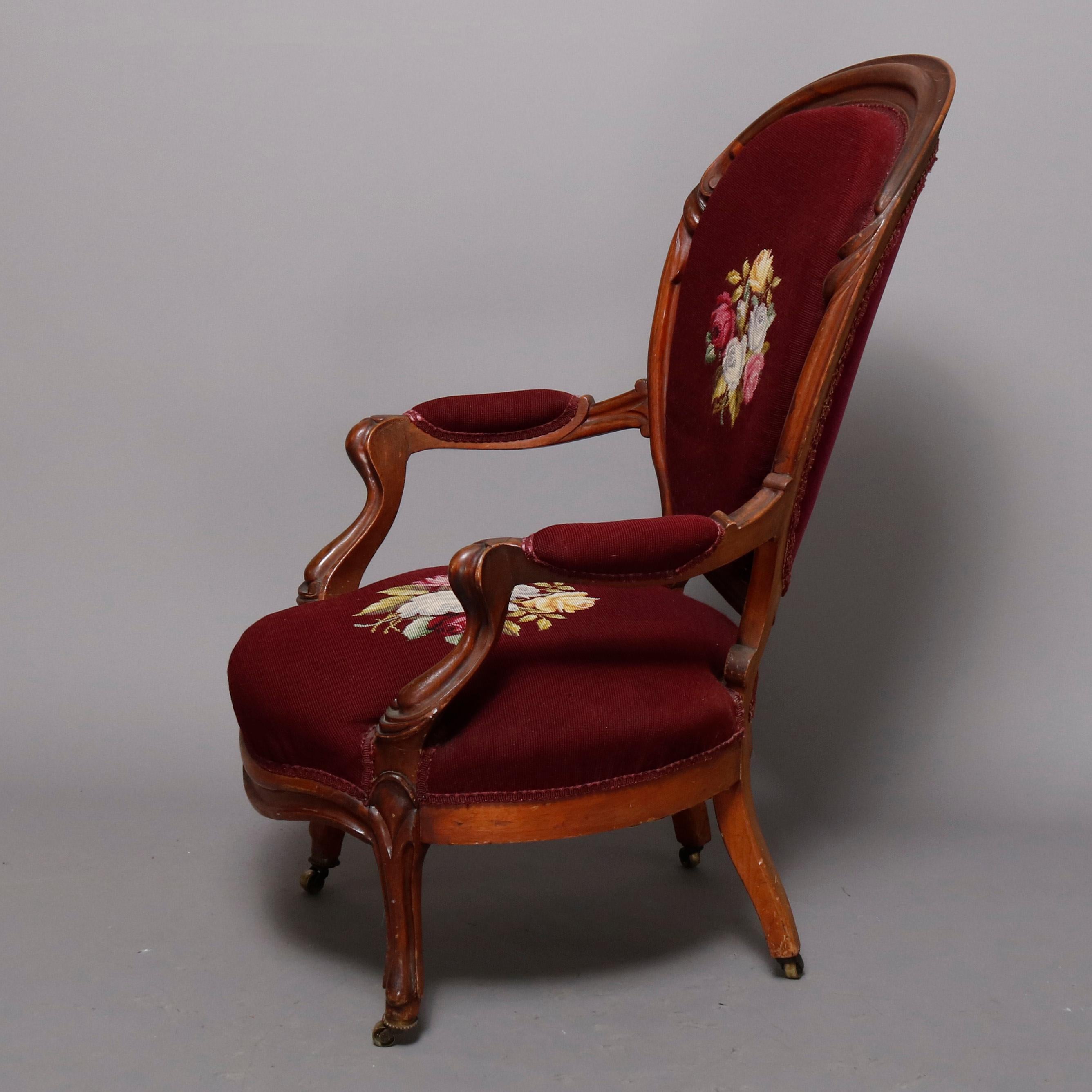 An antique Victorian parlor armchair offers carved walnut frame with balloon back having flanking foliate elements framing needlepoint back with central floral reserve surmounting shaped seat with matching needlepoint cushion, covered and carved