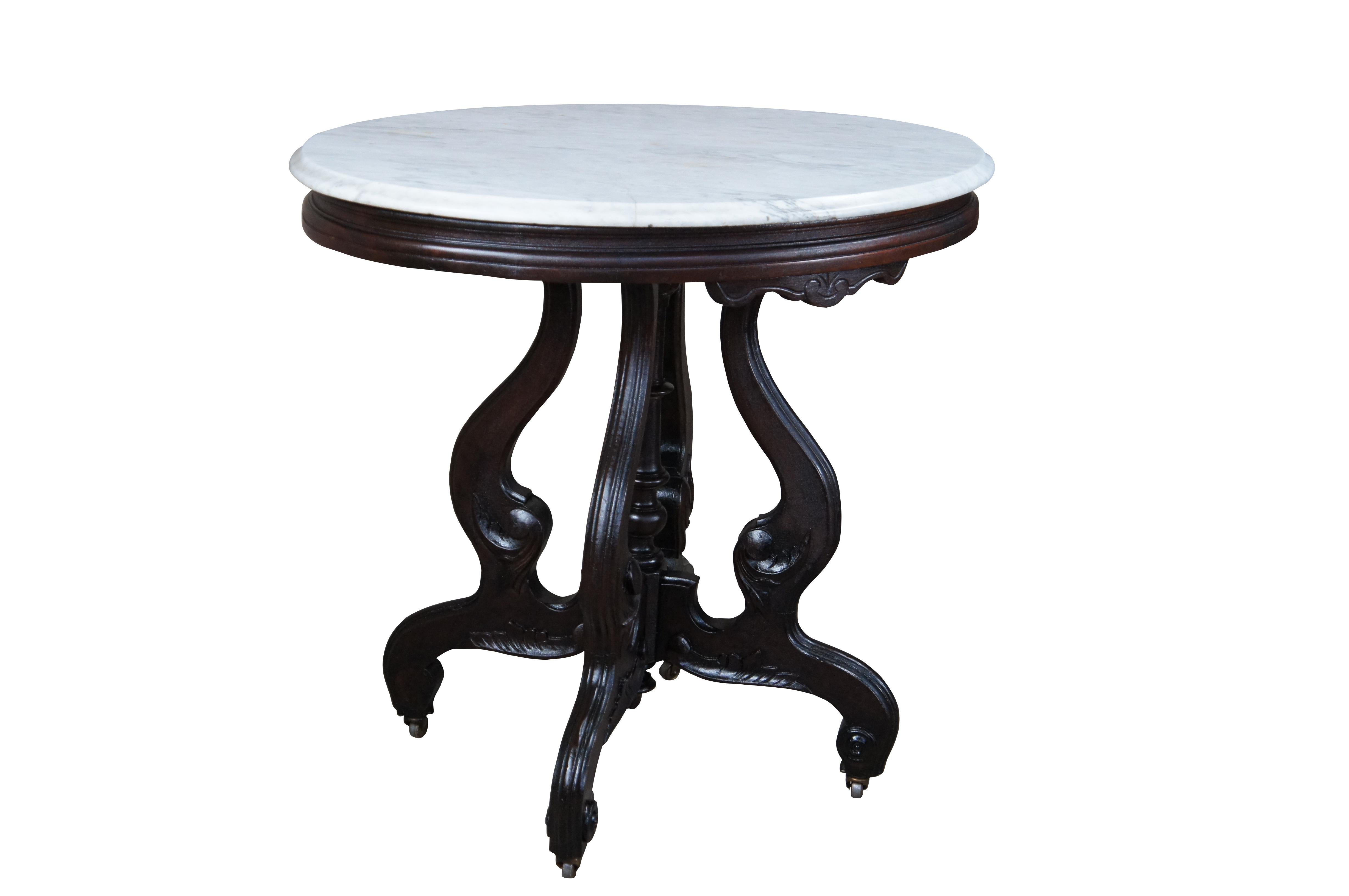 A late Victorian parlor side table.  Features an oval form with white marble top over a serpentine base with carved and scrolled accents.  The table is on casters for ease of movement.

Dimensions:
24