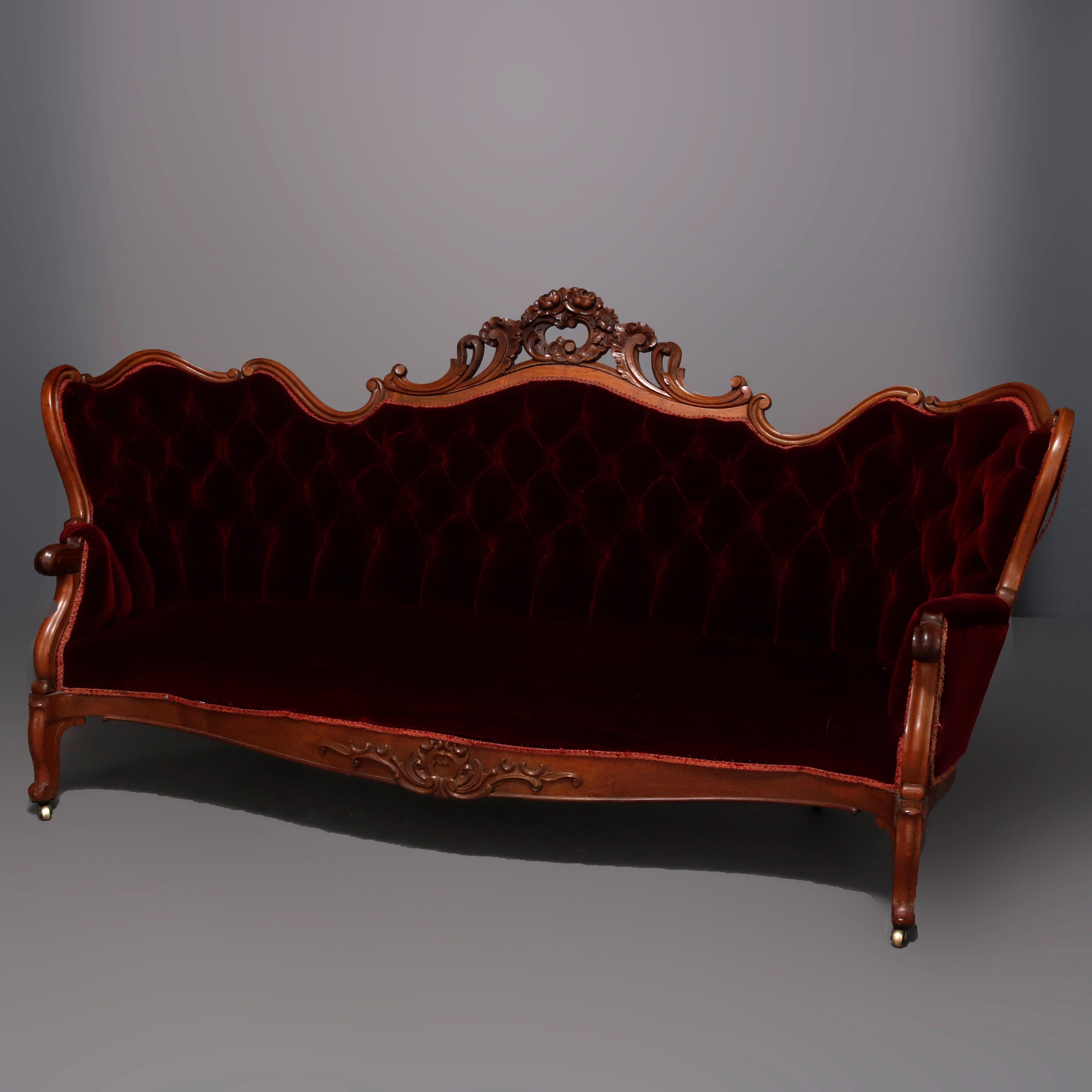 An antique Victorian sofa offers carved walnut frame with shaped back having foliate carved pierced crest over button back plum velvet upholstery, scroll arms and carved apron, raised on cabriole legs, circa 1890

***DELIVERY NOTICE – Due to
