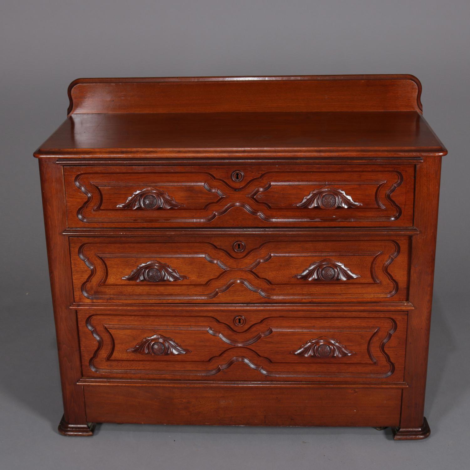 Antique Victorian dresser features walnut construction with shaped and bevelled backsplash over bevelled top and above case with three long drawers having carved panels and nut and leaf pulls, circa 1890.

Measures: 37