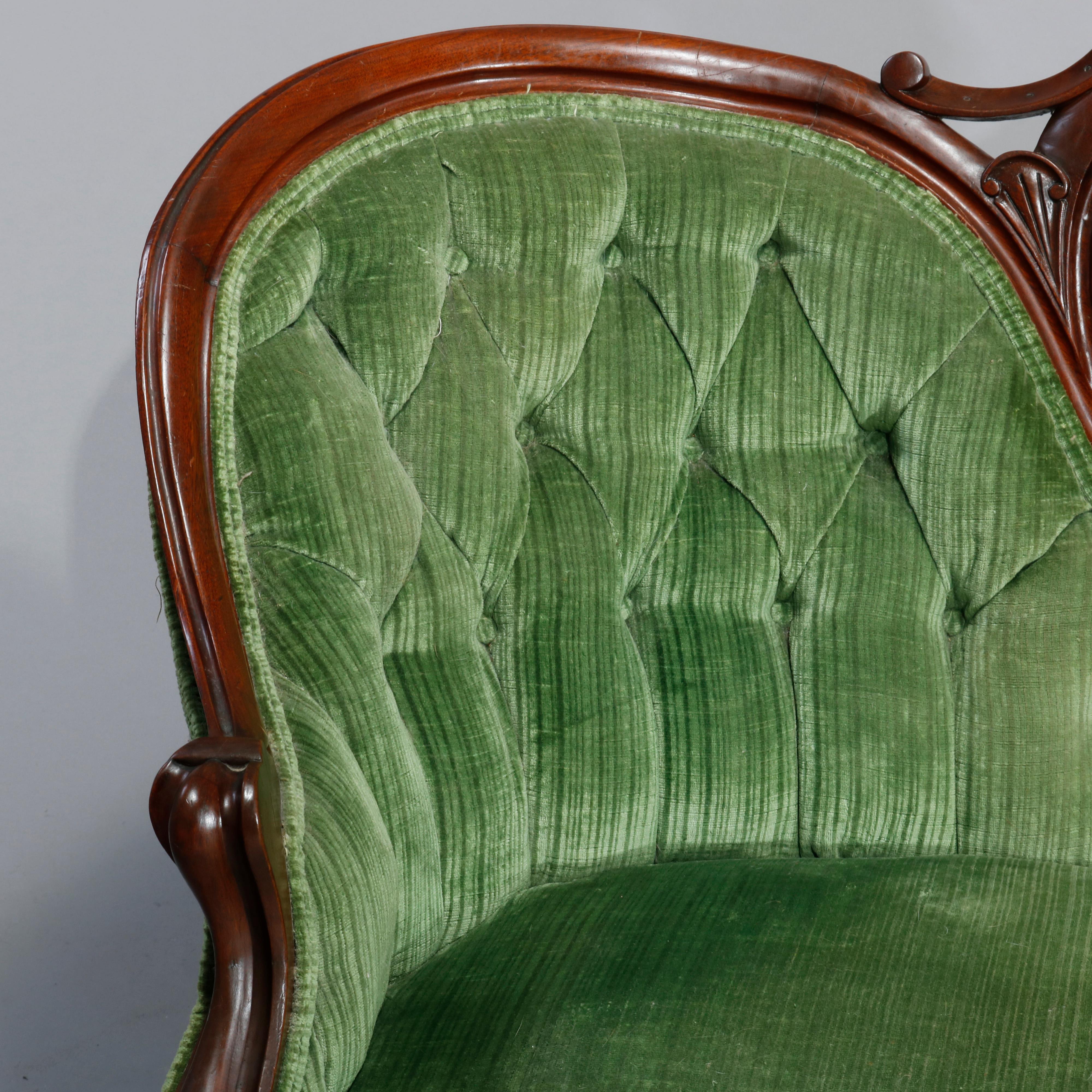 An antique Victorian sofa offers carved walnut frame in medallion and curved back form with foliate crest over button back with scroll form arms and raised on cabriole legs, c1890.

Measures: 40