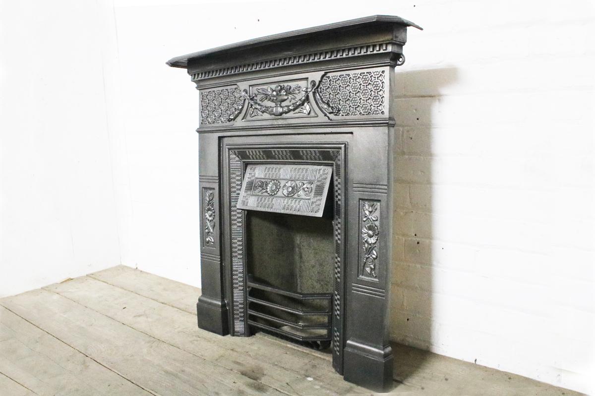 Antique ornate cast iron Victorian bedroom fireplace. The fireze decorated with a laurel sway supporting a classical urn overflowing with fruit and ears of corn flanked by an interconnected hexagonal geometric pattern. Recessed panels to the jambs