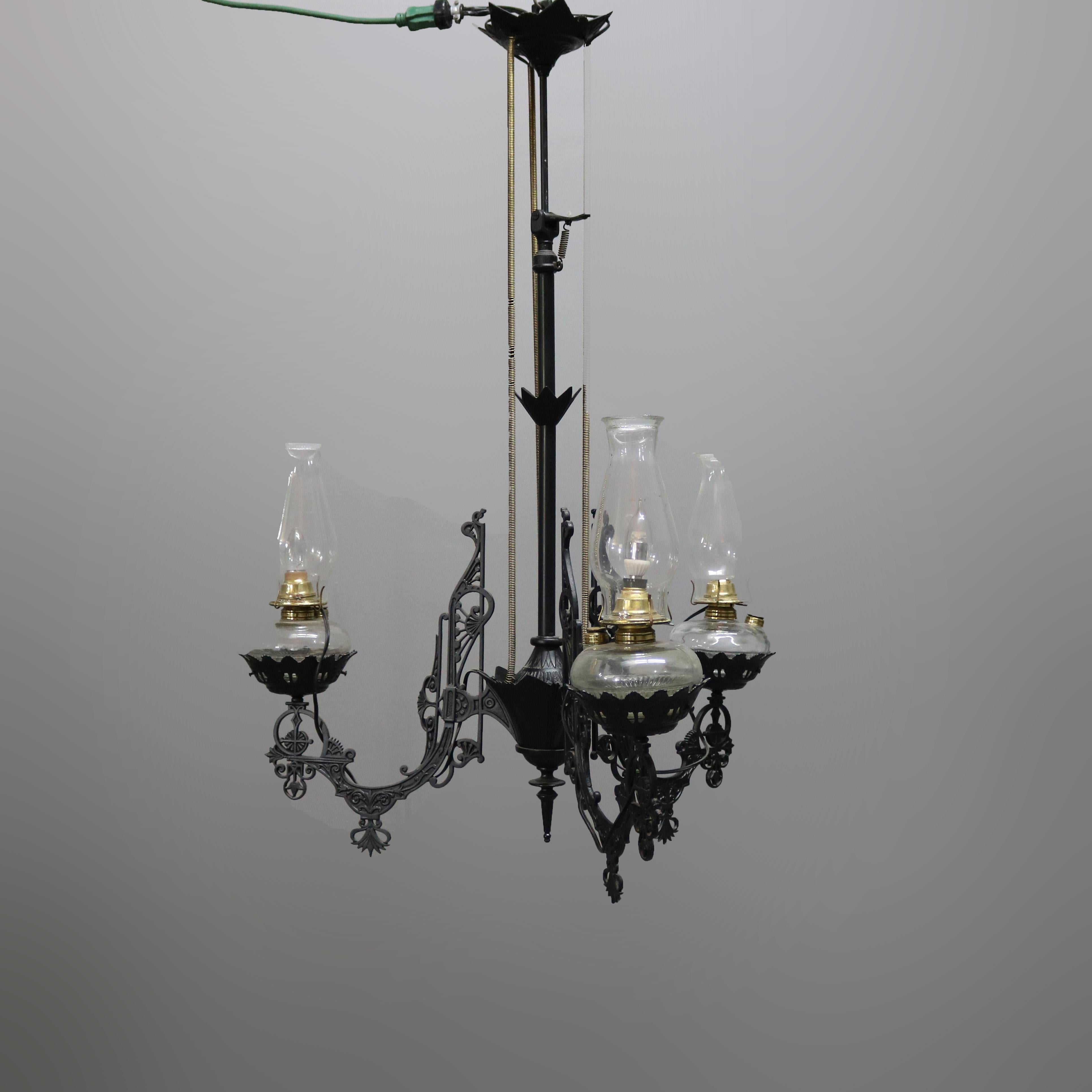 An antique Victorian iron horse hanging light offers cast iron construction with three arms terminating in electrified lights with glass shades, 19th century. 

Measures: 44