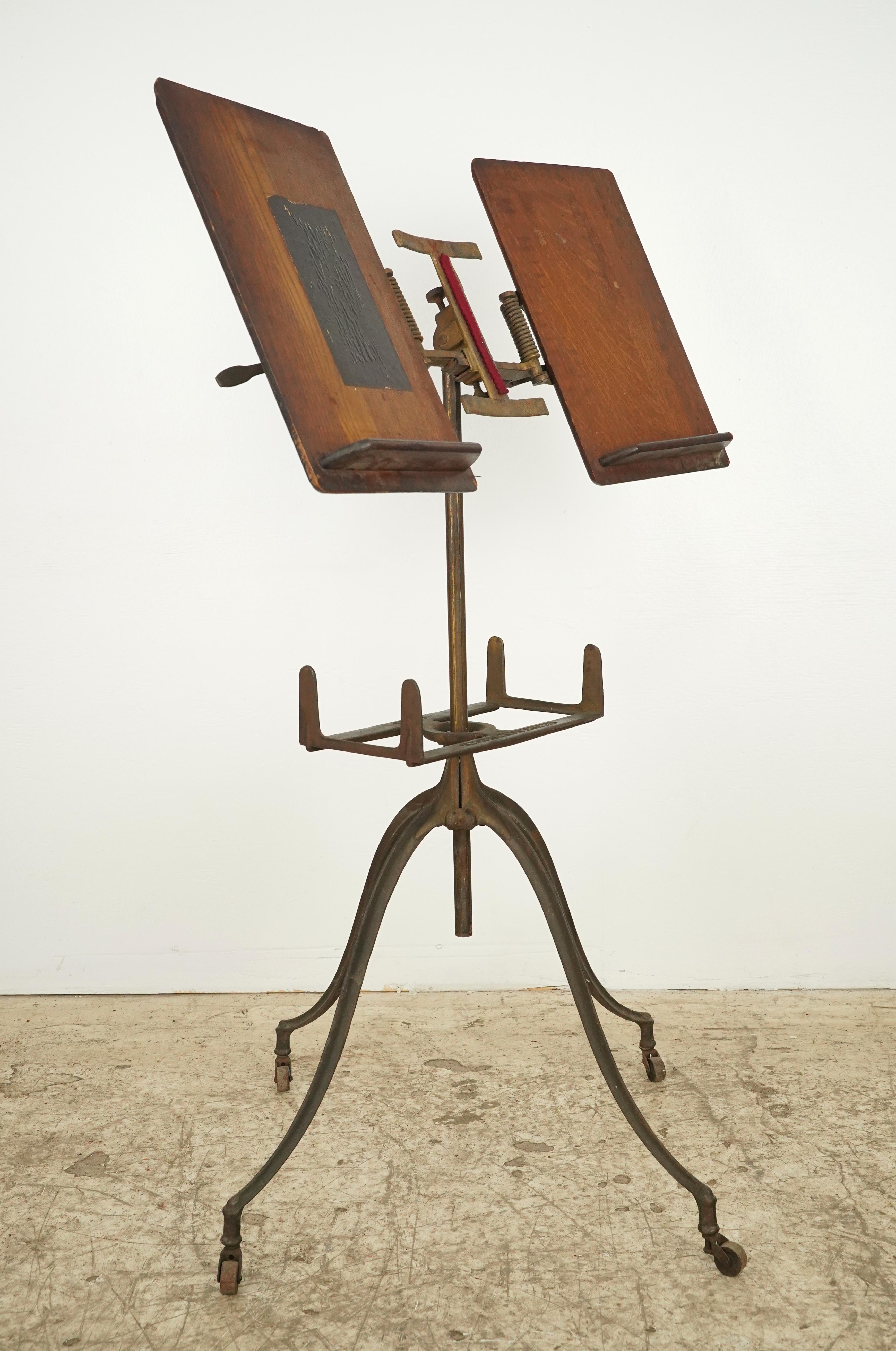 Antique 1890s dictionary stand with a cast iron base featuring four curved legs ending in small casters. The top features two adjustable oak book rests, designed to hold large books like dictionaries. It includes a mechanism for adjusting the
