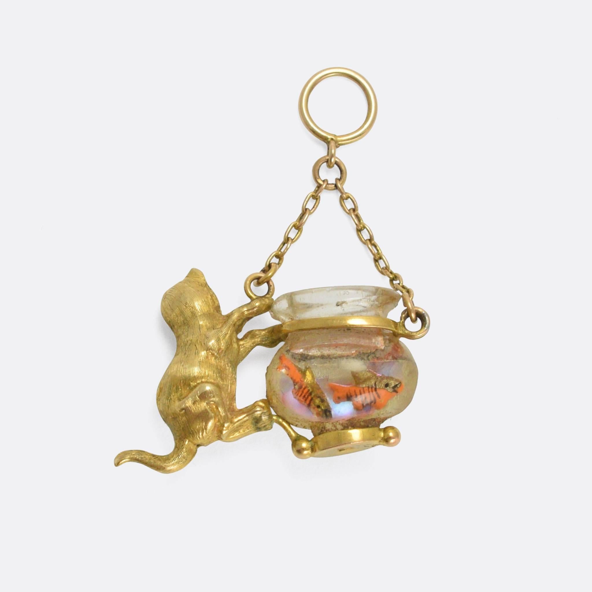 A cute antique novelty pendant, modelled as a golden cat eyeing up a goldfish bowl. The kitty is beautifully detailed, and has been set with emerald eyes, while the bowl is made from moulded glass that has been cleverly reverse carved with fish and