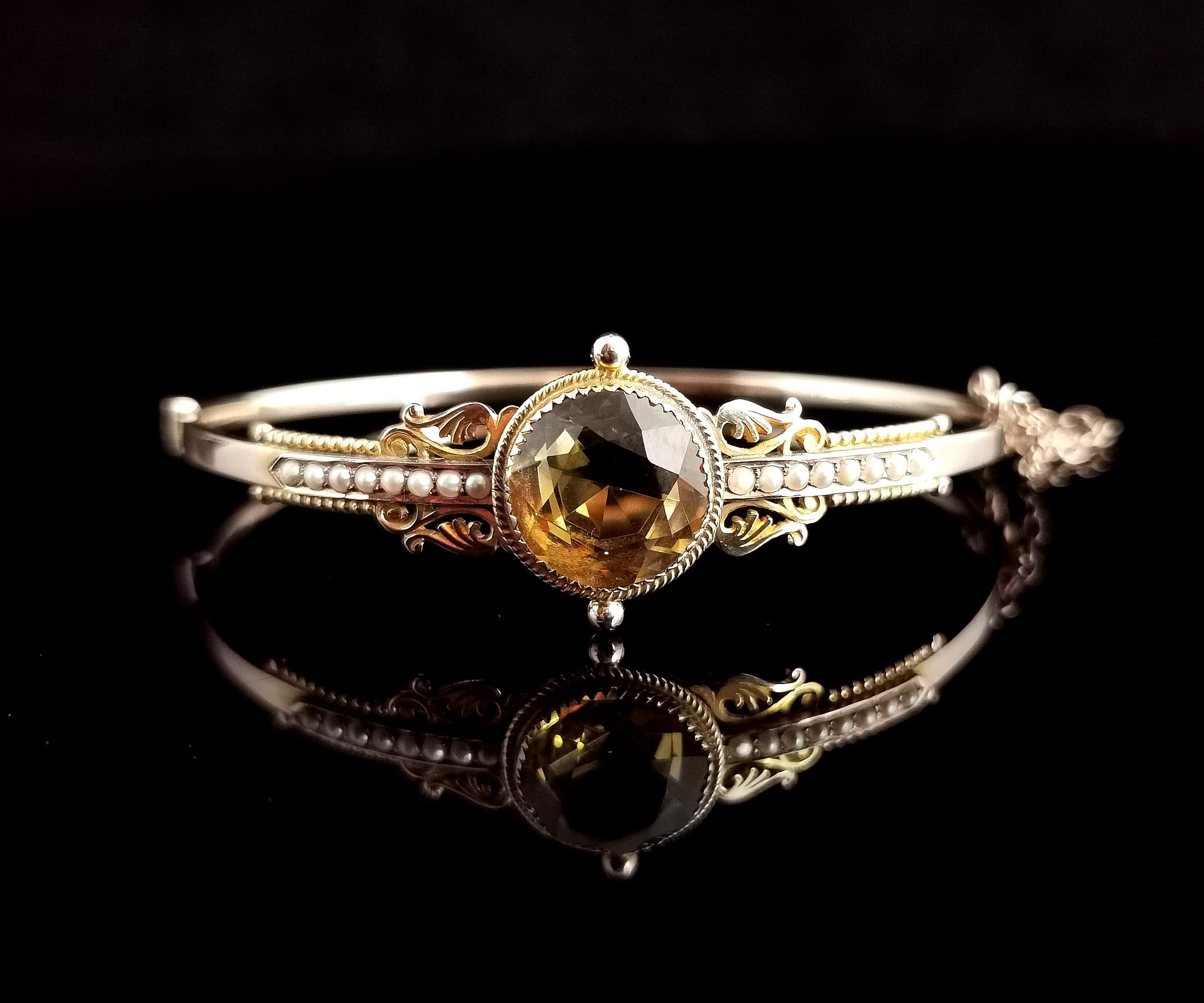 A beautiful antique, late Victorian era, 9 karat yellow gold, Citrine and seed pearl bangle.

A pretty piece with Etruscan revival vibes, it has a large round cut rich yellow citrine set centre front with rows of creamy seed pearls either side.

The
