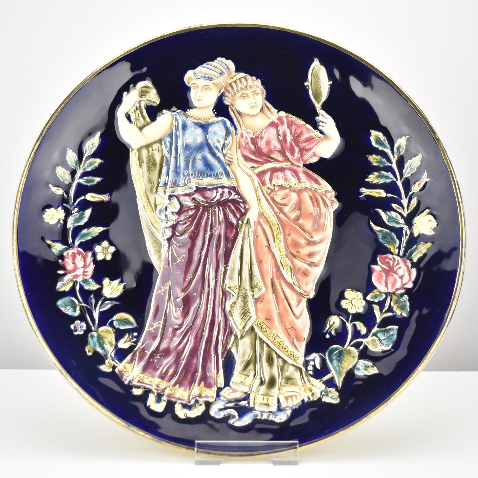This large and exquisitely detailed Victorian majolica wall-hanging relief plate features a striking depiction of two elegantly adorned Greek goddesses. Created in a vibrant Barbotine Greek Revival style with richly hand-painted polychrome
