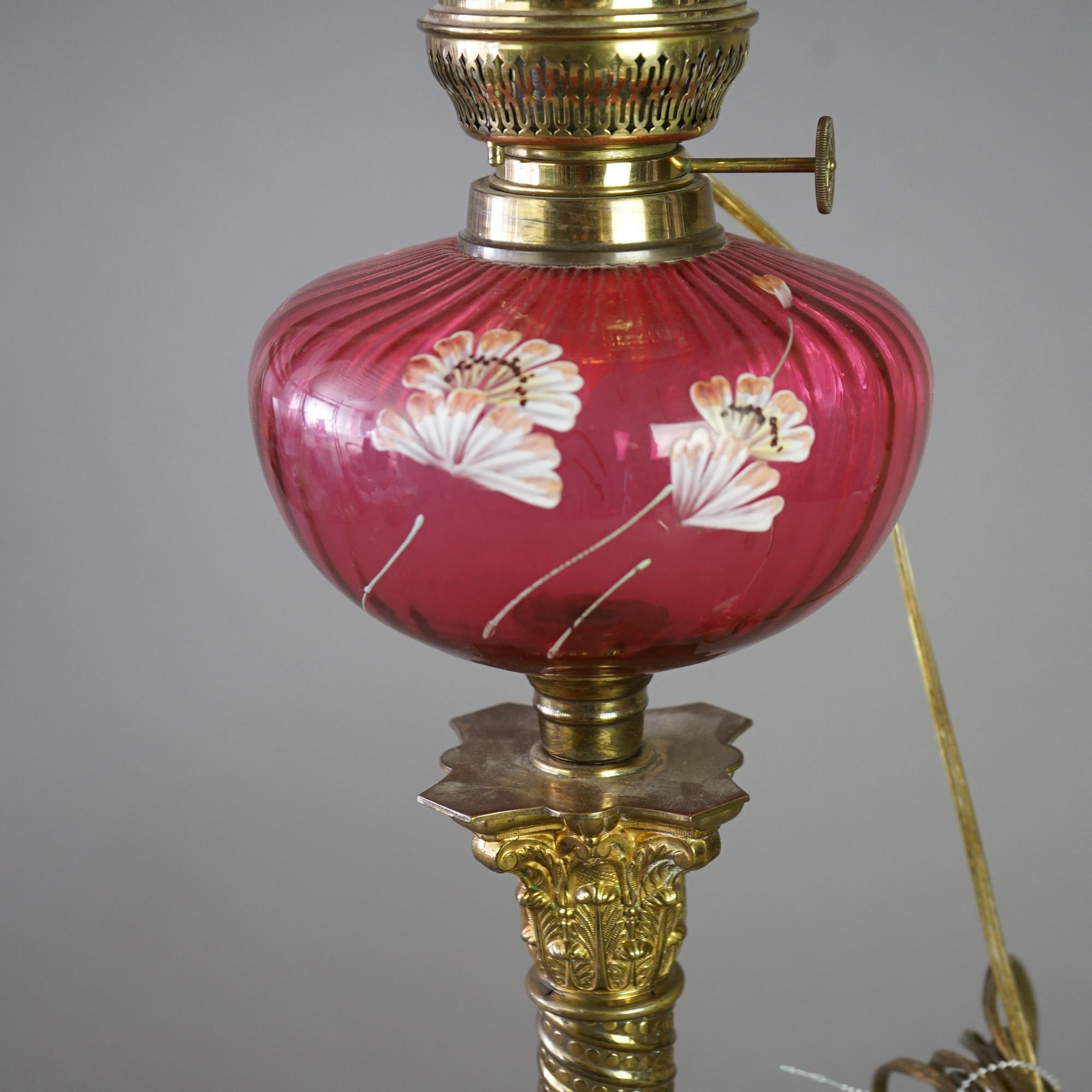 An antique Victorian banquet lamp offers cranberry glass ruffle rim shade over base having matching glass font with hand painted flowers, raised on brass Corinthian form column, electrified, C1890

Measures - 30.25