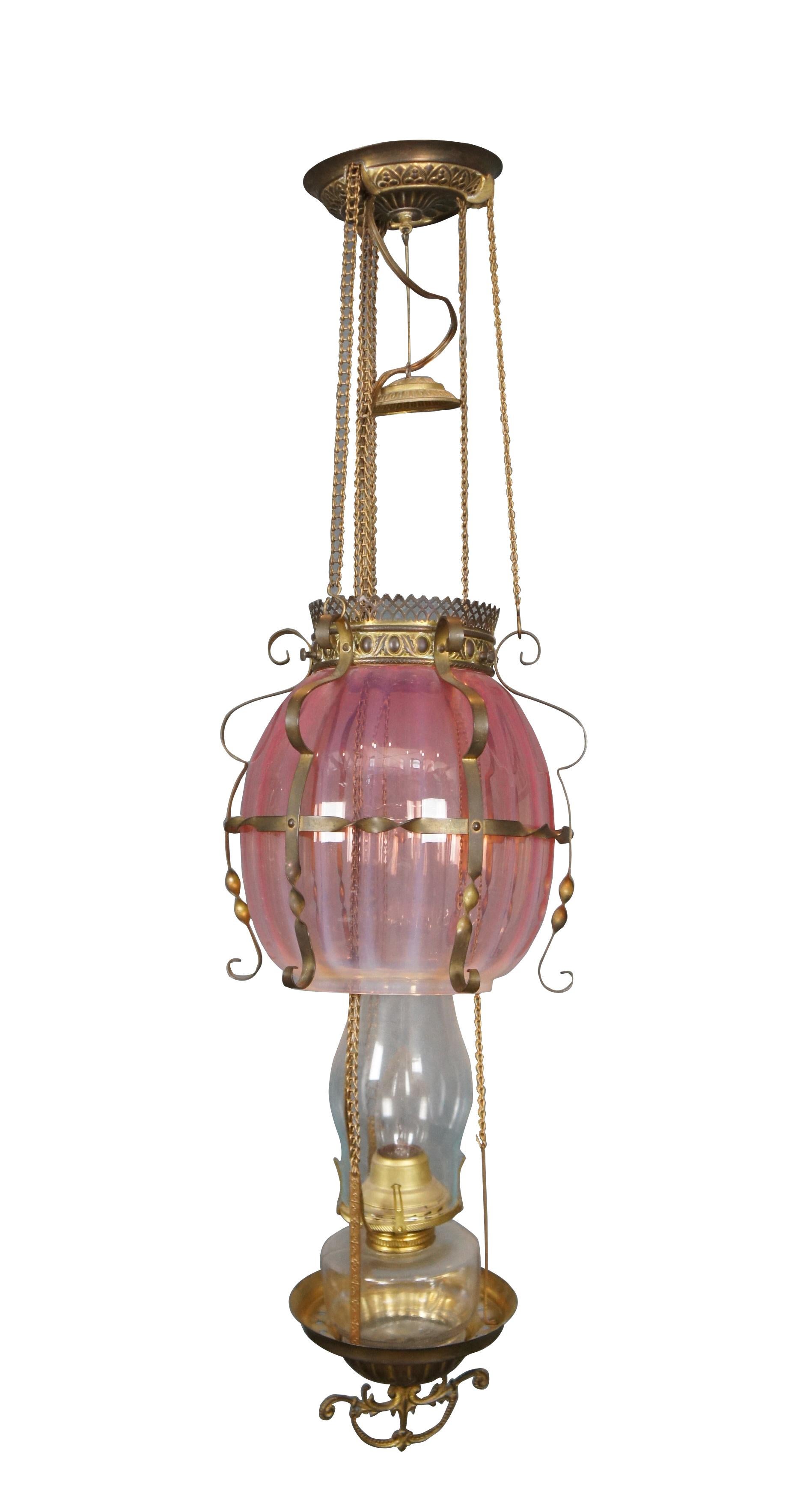 Late 19th century converted oil swag hurricane pendant light / chandelier. Repousse brass base with ornate finial, collar and smoke bell; scrolled / twisted brass cage around a fluted opalescent cranberry glass shade. Suspends from patterned ceiling