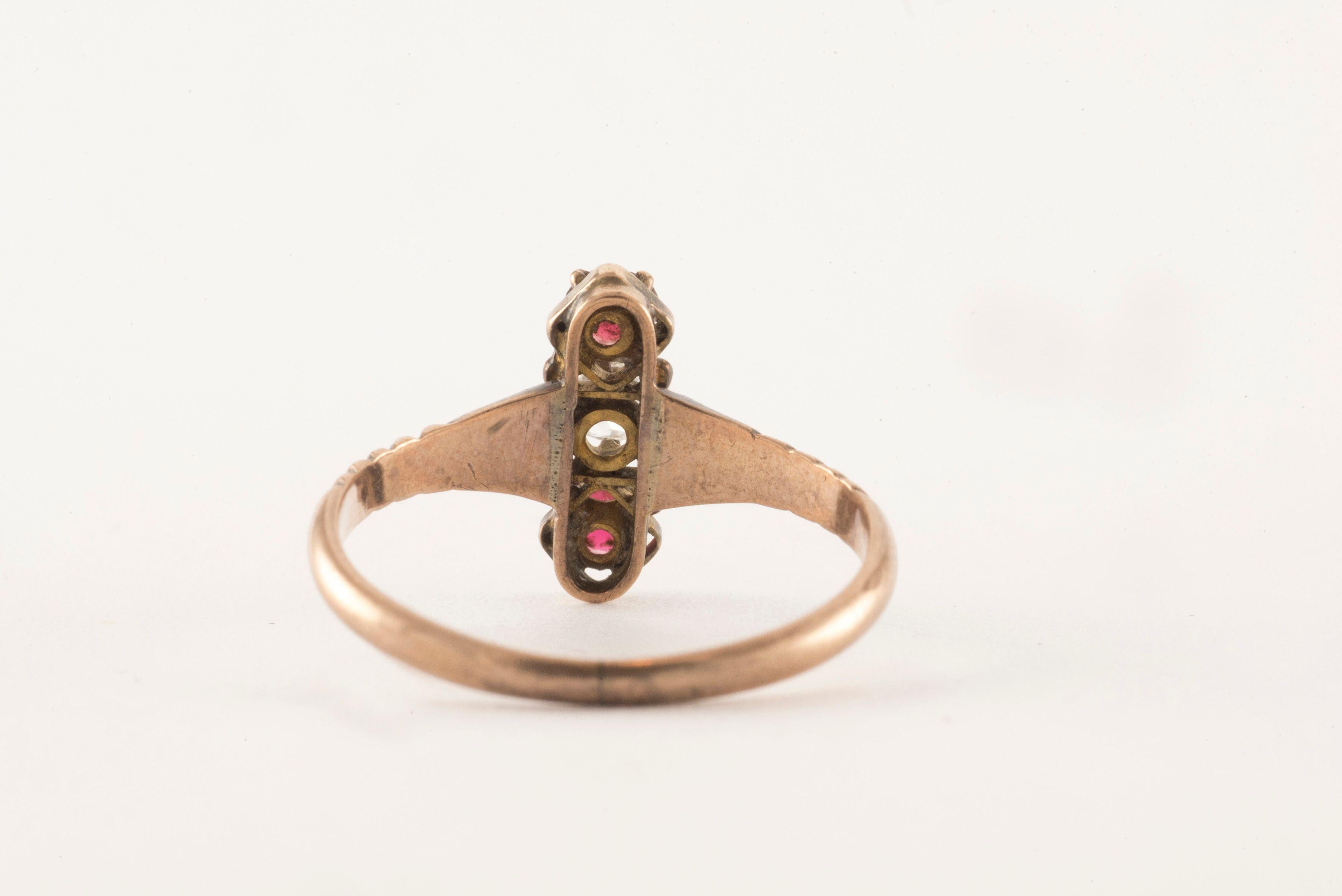 An Old Mine cushion cut diamond measuring approximately 0.15 carats, H color, VS clarity, sits at the center of this three-ring band fashioned from 10kt rose gold and accented by two round-shaped red garnets. The vertical orientation of this ring is