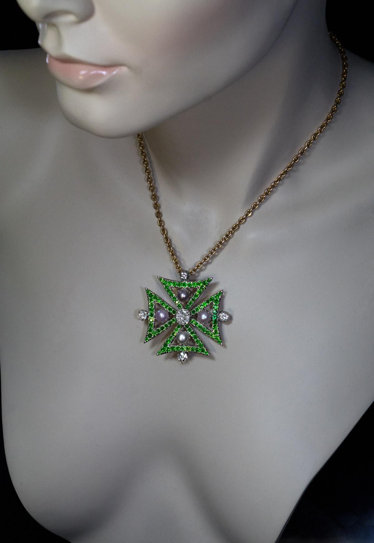 Circa 1880s

This magnificent Victorian era pendant / brooch is designed as a large Byzantine (frequently called Maltese) cross set with bright white diamonds, gray pearls, and vivid green Russian demantoid garnets. The cross is handcrafted in