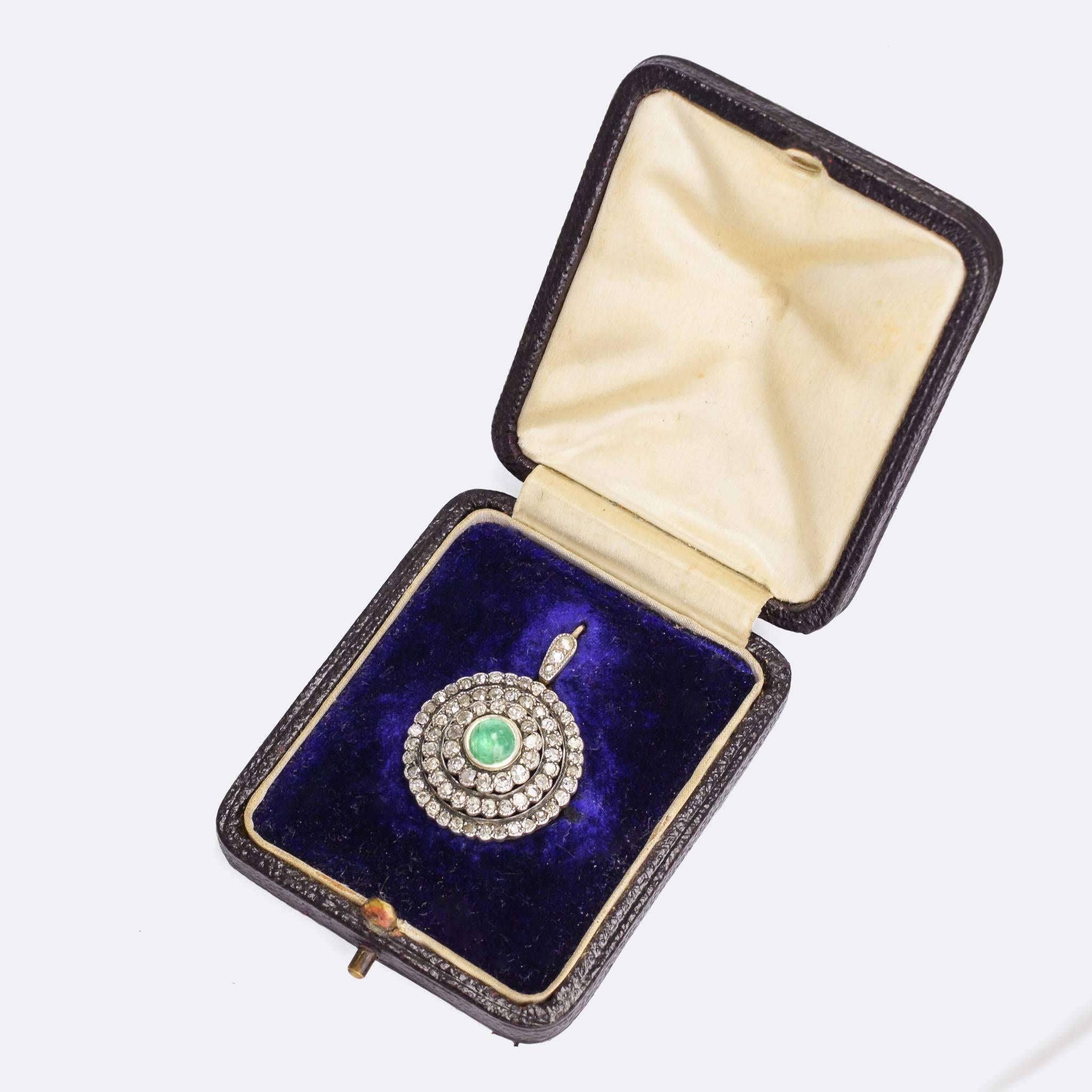 A fine quality diamond cluster pendant, three rows of old cut diamonds surround a natural emerald cabochon. Set in 15k gold with silver settings. The piece comes in its original fitted box. There are also removable brooch fittings that attach to the