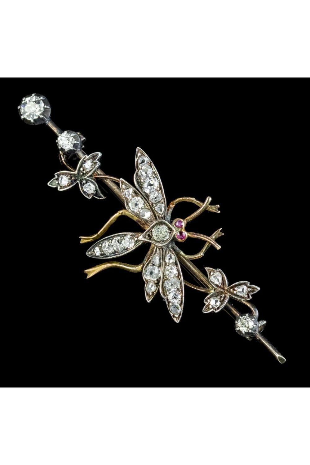 A stunning Antique late Victorian brooch featuring a large, winged insect decorated with sparkling Old Mine cut Diamonds and red cabochon Ruby eyes. It’s perched on a long bar set with further Mine cuts and leaves and can be turned left or right on
