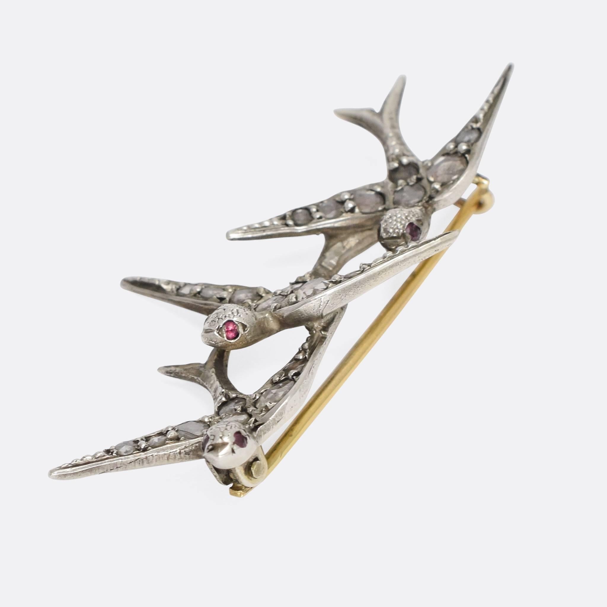 A beautiful antique brooch featuring three swallows set with rose cut diamonds and ruby eyes. The birds have been expertly crafted with lovely detailing and perfectly capturing the motion of flight. The stones are set in silver, with a light gold