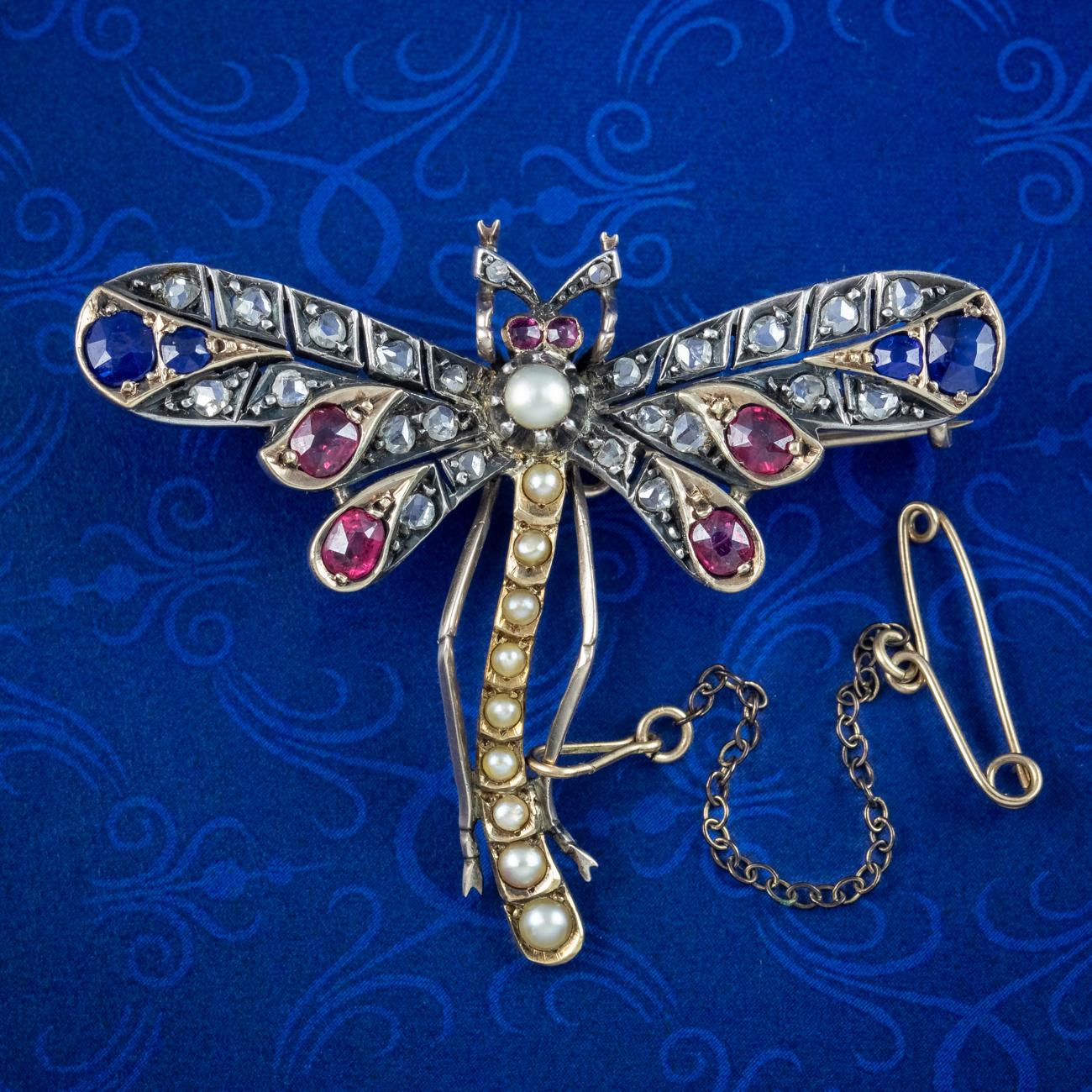 A colourful antique Victorian dragonfly brooch decorated with an array of coloured gemstones across the front, including blue sapphires, pink rubies and twinkling rose cut diamonds with a row of natural pearls running down the length of the body and