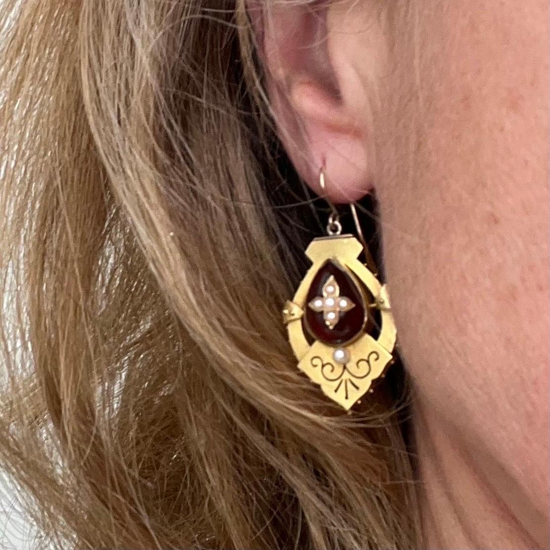 A beautiful and romantic example of Victorian jewelry design, this pair of antique 9 karat gold dangle earrings is masterfully crafted with richly detailed ornamentation and symbolic stones. These earrings capture the essence of 19th-century style