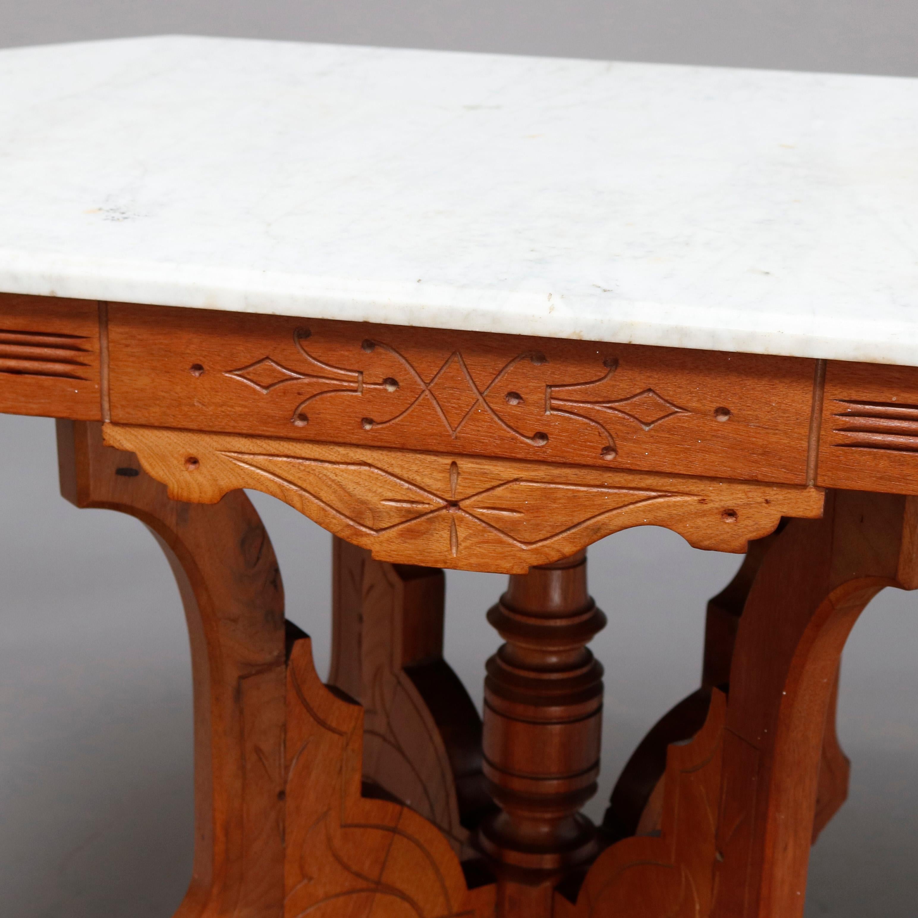 An antique Victorian Eastlake side table offers a beveled clip-corner rectangular marble top surmounting carved walnut frame having shaped and incised skirt, raised on shaped legs with drop ball finials and central turned column having drop finial,