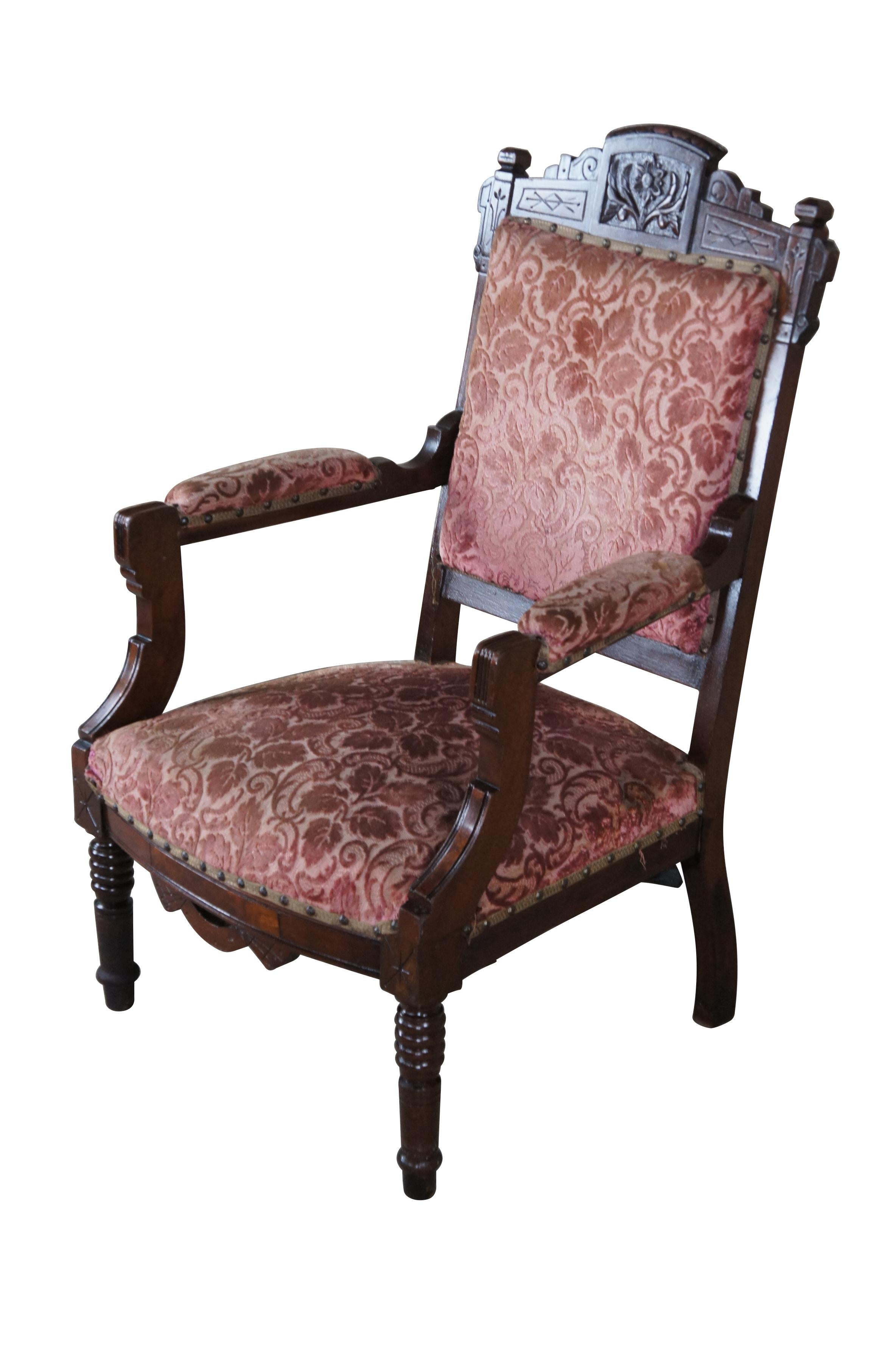 A lovely Victorian arm chair, circa last quarter 20th century.  Features classic Eastlake styling with a scrolled and carved back, padded down swept arms, burled panels and turned ribbed legs.  The chair is upholstered in reddish raised velvet leaf