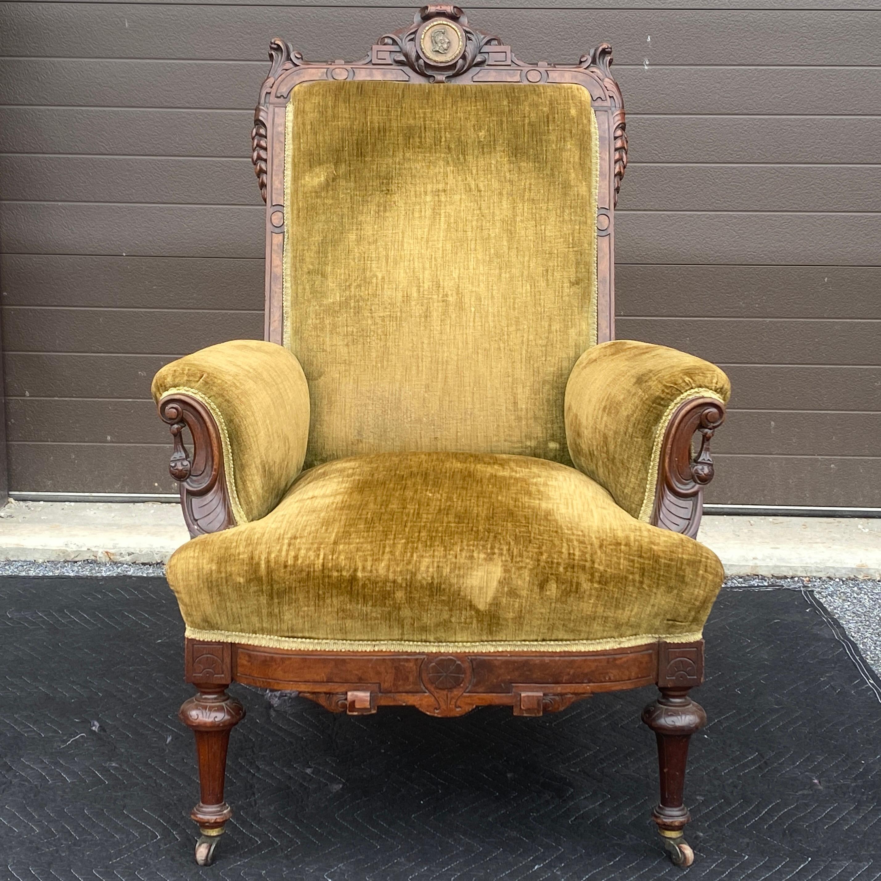 Antique renaissance revival lounge chair featuring a finely carved carved walnut frame, a bronze medallion at the crest, and brass casters with wooden wheels on the front legs. Attributed to John Jelleff & Co Newark NJ. Previously reupholstered. 