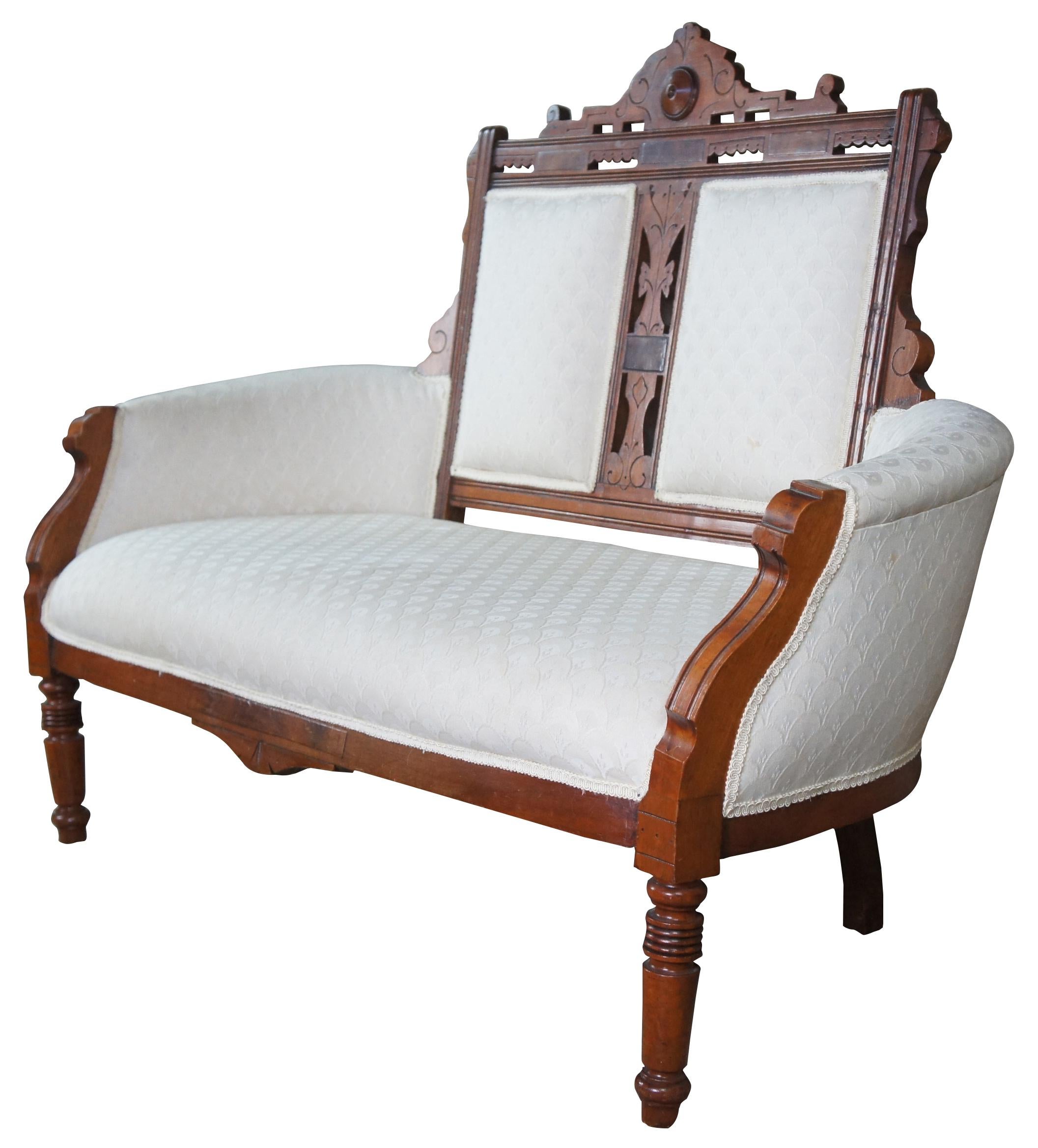 Antique Victorian Eastlake parlor settee or love seat. Made of walnut featuring a flare of Renaissance Revival with carved pierced back and frame with turned legs supporting a wide frame and white upholstery. Measure: 55