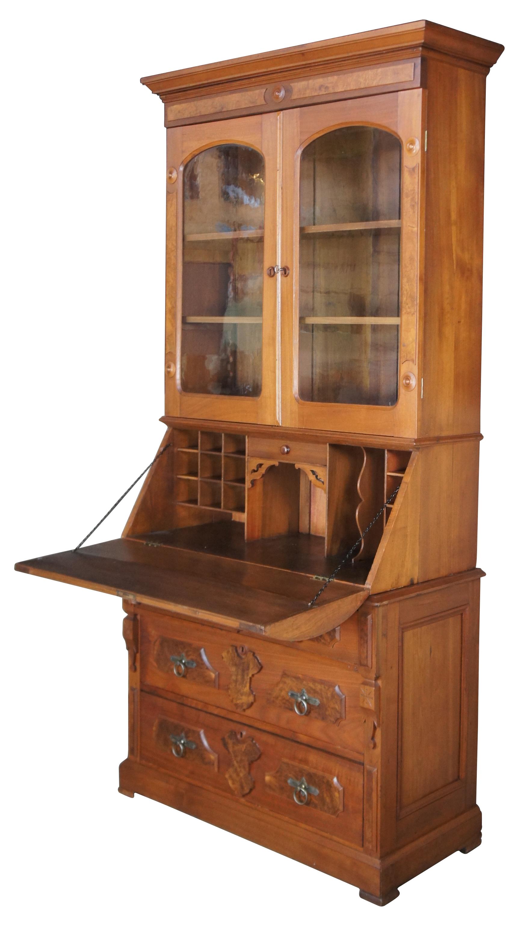 An exquisite antique Victorian Eastlake drop front secretary desk and bookcase; circa 1880s. Made of solid walnut accented in crotch walnut. Features a unique form having the appearance of a half cylinder desk with hutch and three lower drawers.
