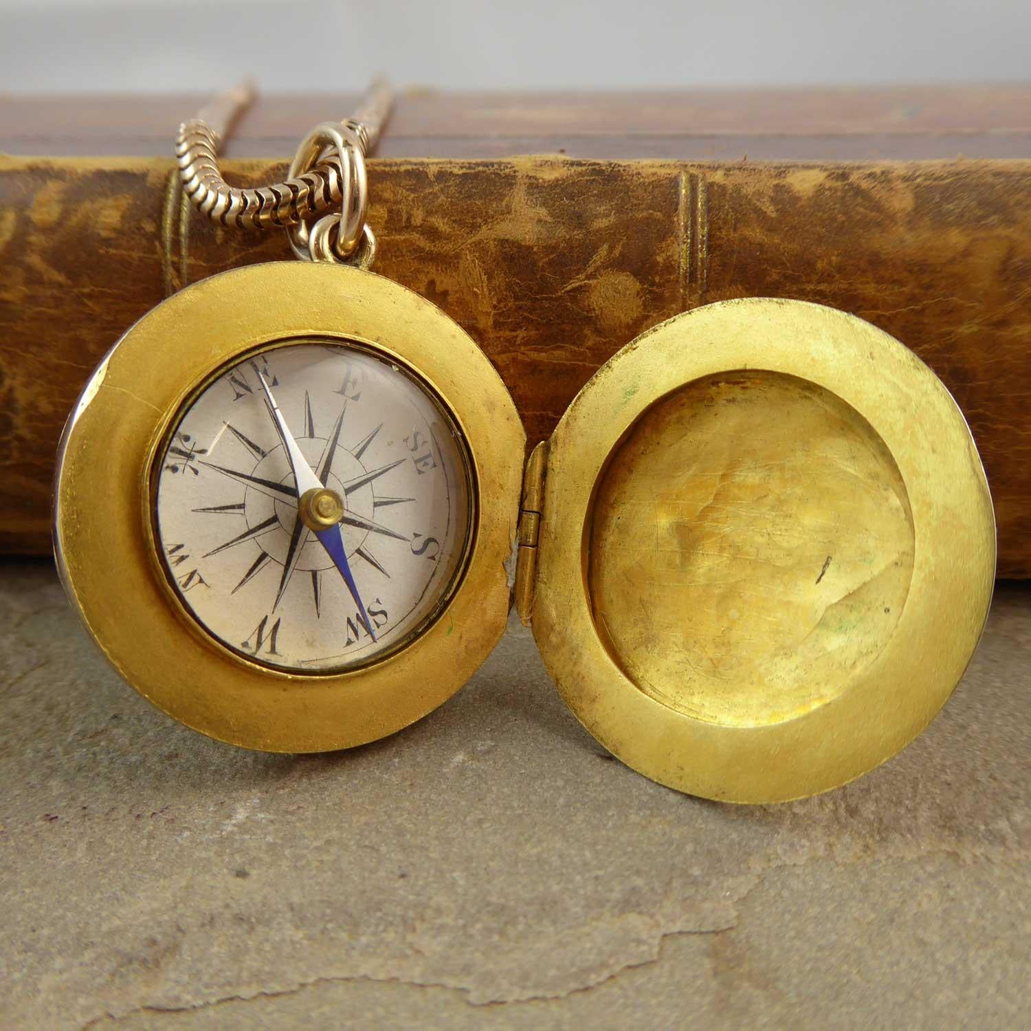 An antique gold locket of unusual design having one half opening to reveal and portrait/keepsake compartment and the other half opens to reveal a compass. Circular in shape and with a slight dome, both the front and back of the locket have a pretty