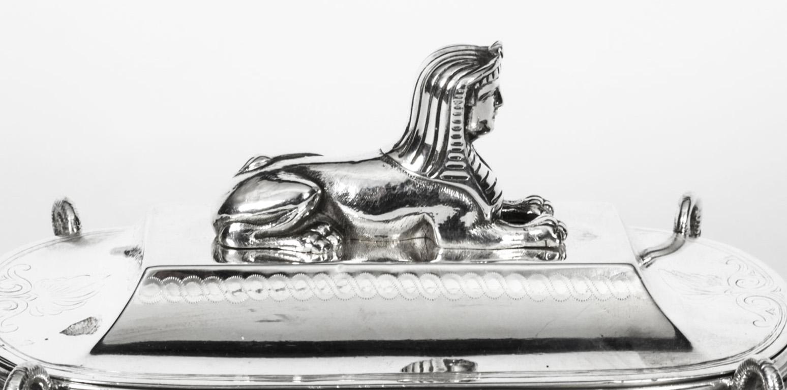 This is a elegant antique Victorian silver plate lidded inkwell Standish, late 19th century in date.
 
The ink stand is in the form of an Egyptian sarcophagus which features a sphinx mounted lid on a large oval base raised on scrolled foliate