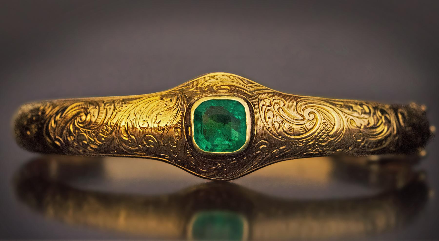 Circa 1890

This antique 14K gold hollow bangle bracelet is finely hand-engraved with scrolling foliage in the Neo-Rococo style. The bracelet is bezel set with an emerald cut natural emerald of a saturated bluish green color. The emerald (likely of