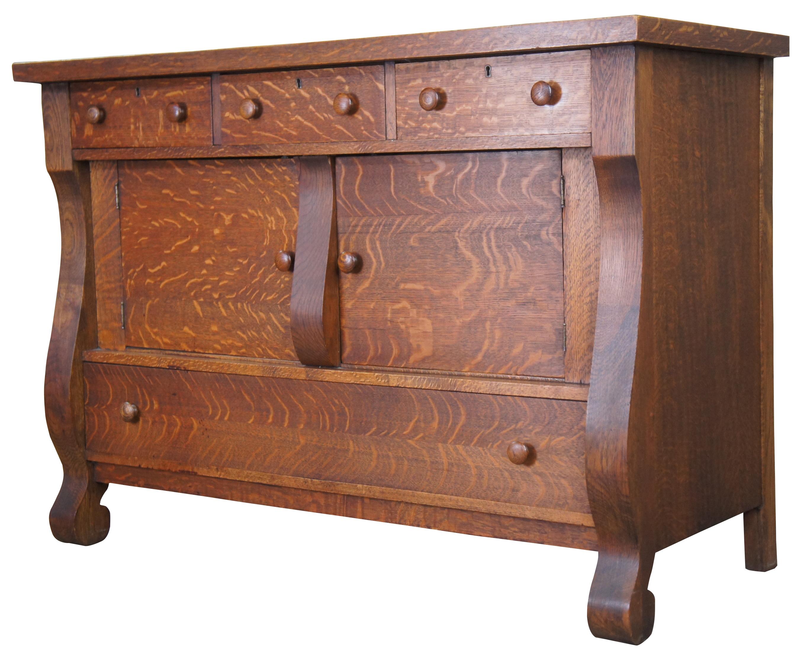 Early 1900s quartersawn oak buffet or server. Features a rectangular form with robust outer legs leading to scrolled feet. Includes three upper dovetailed drawers, a large central cabinet and full size lower drawer. Measure: 54