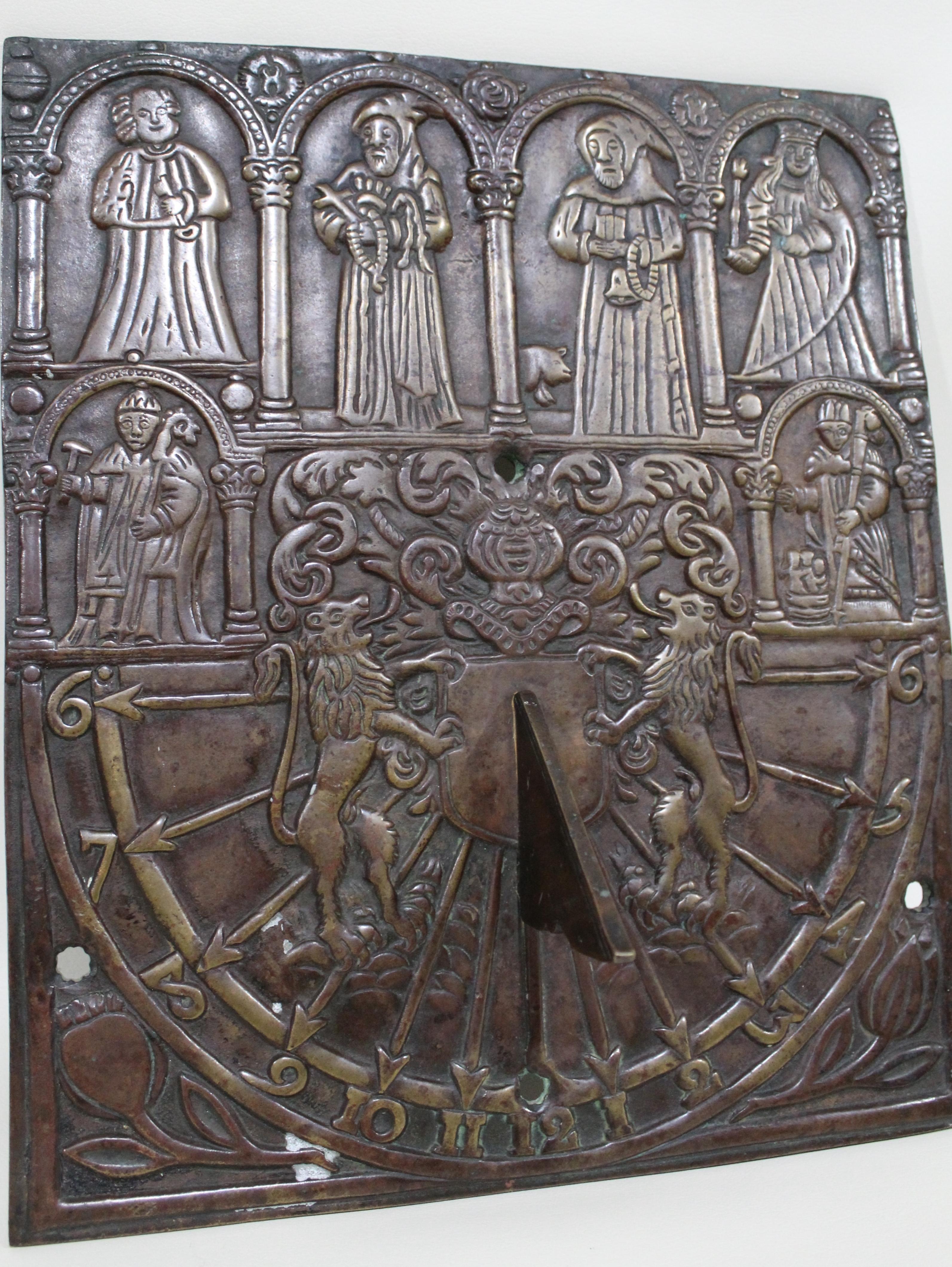 Presumably having English origins, this antique solid bronze sundial is ornately cast with a series of Medieval figures across the top portion and standing in the facade of an arched building. Underneath are two smaller Medieval figures, also