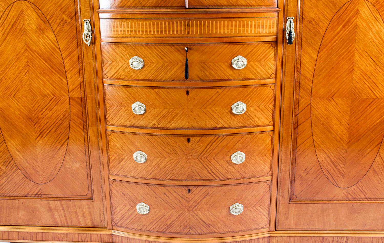 This is a large and impressive English antique Victorian Sheraton Revival satinwood inlaid wardrobe, circa 1880 in date.
 
The central section has a pair of cupboard panelled doors opening to a central shelf above five graduated drawers with a