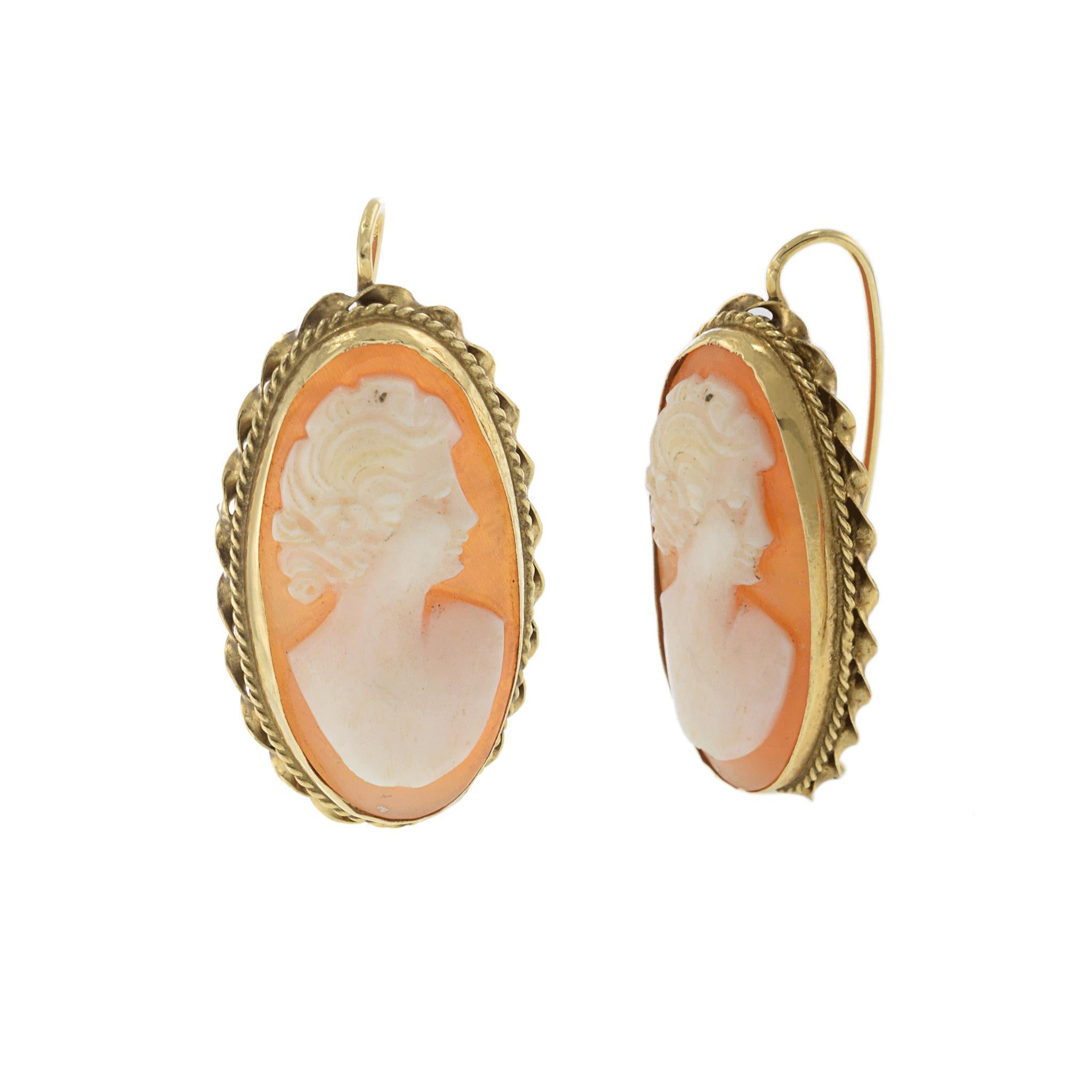 These antique Victorian-era earrings feature hand-carved shell portrait cameos set in ornate 14KT yellow gold frames. Each oval cameo depicts a classical female profile in soft coral and ivory tones, reflecting the fine artistry of 19th-century