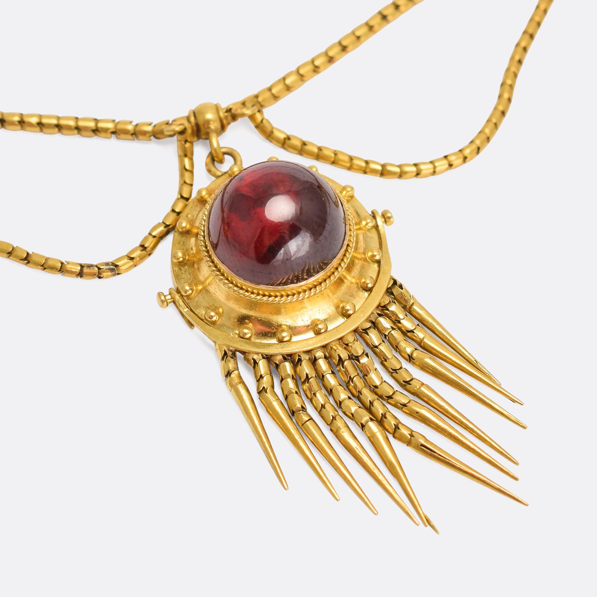 This superb antique swag necklace was made in the 1860s, crafted in the Etruscan Revival style. The three main drops - each set with a bright garnet cabochon - feature applied ropework details and flexible gold fringes. They hang from a snake link