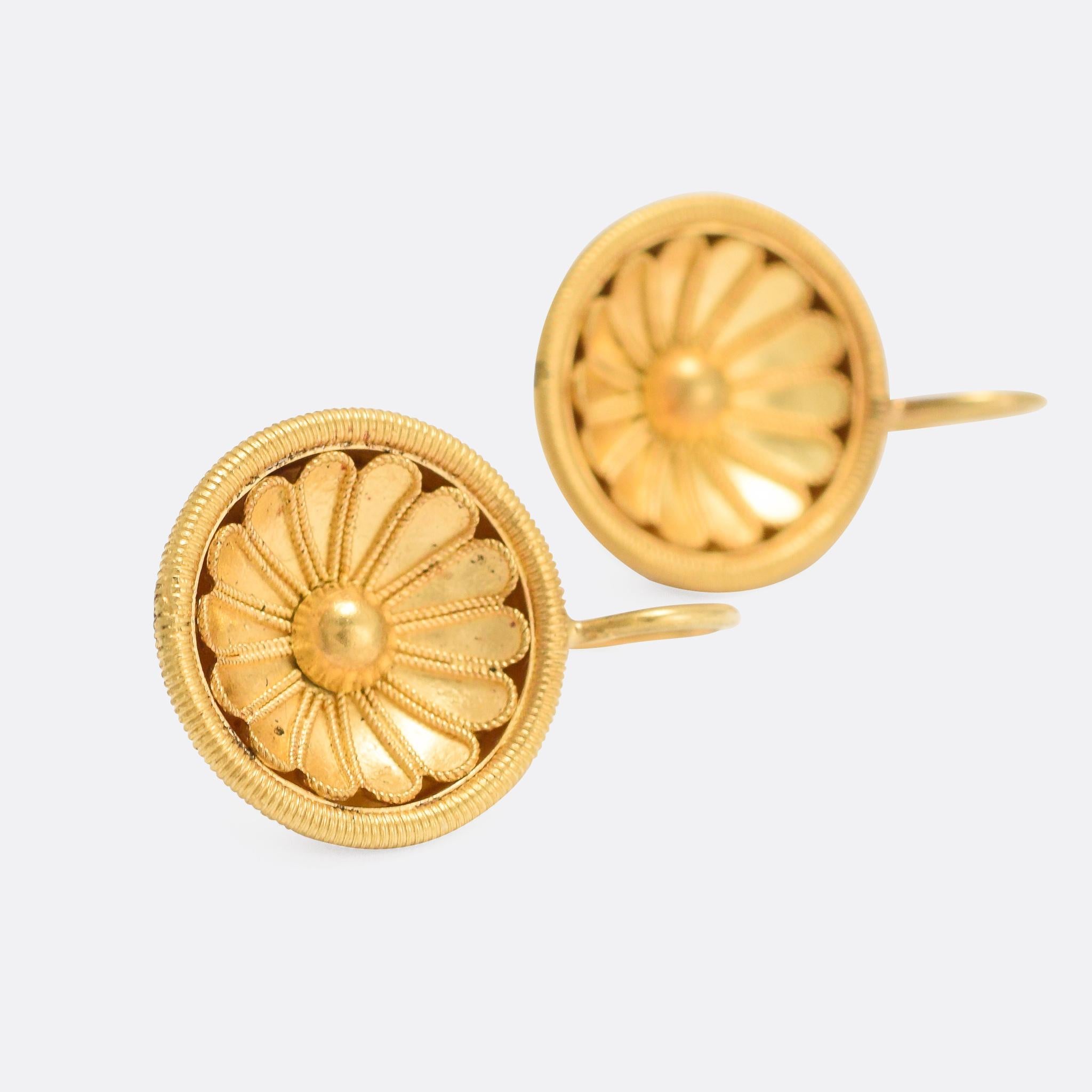 A fine pair of antique earrings crafted in the Etruscan Revival style. The date from circa 1870, modelled as stylised, dish-shaped flowers within a ribbed gold halo. They're fashioned in 15 karat yellow gold and reminiscent, in style, of