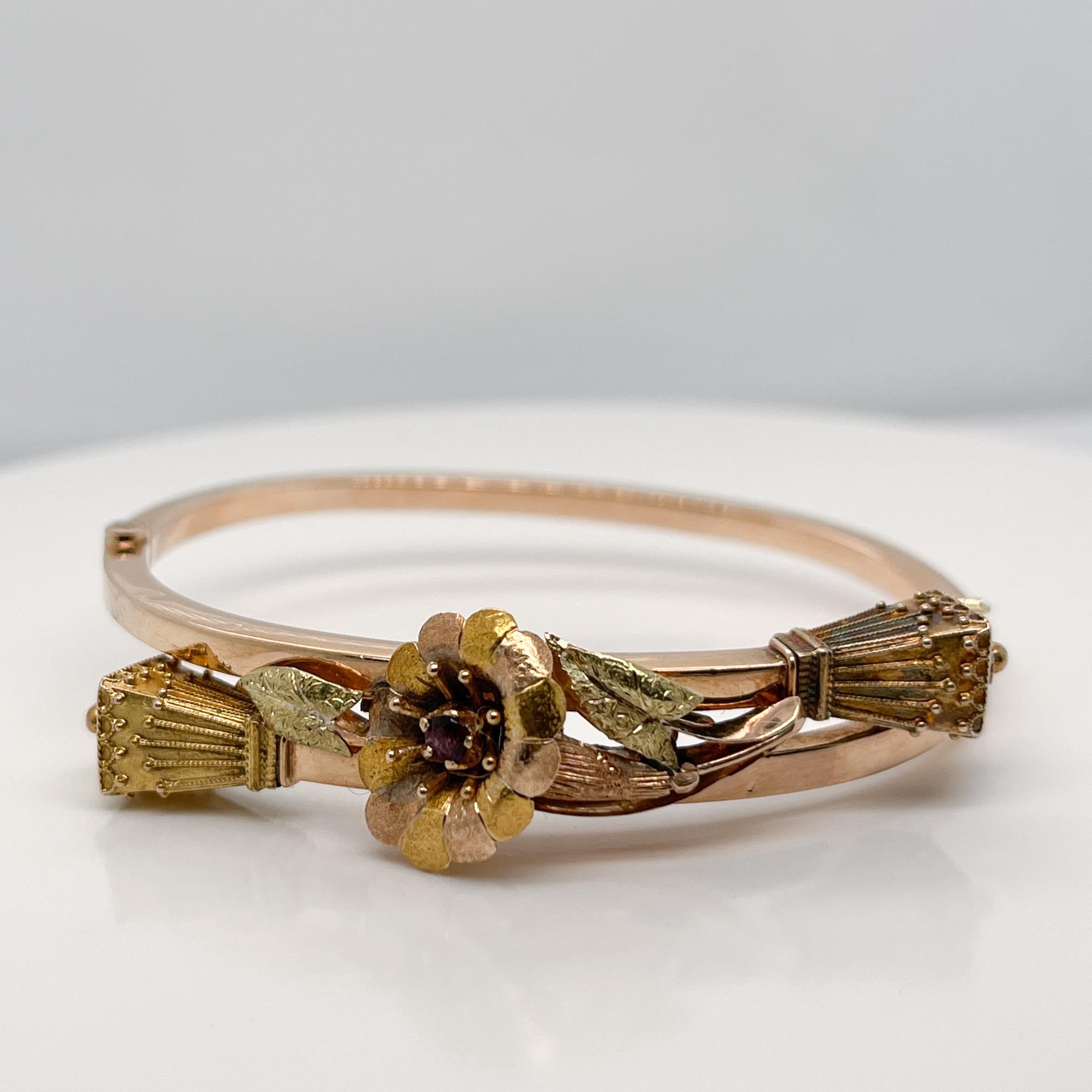 A very fine antique late Victorian bangle bracelet. 

Fashioned in rose and yellow gold as a hollow, square shaft bracelet that is centered on a figural flower (likely a Lily). 

The lily is prong set with an amethyst and flanked by two leaves on