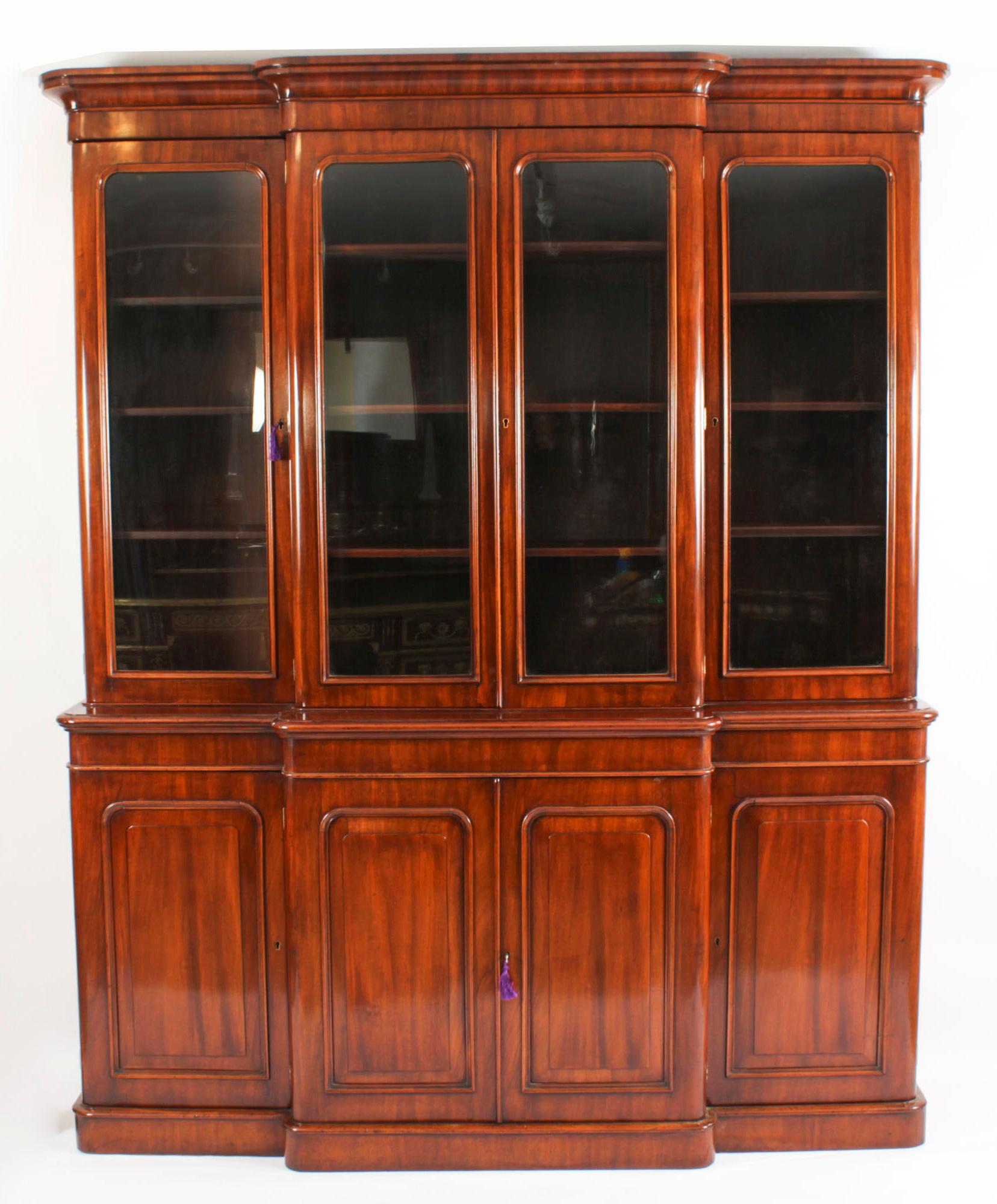 This is a beautiful antique Victorian breakfront bookcase, masterfully crafted in rich figured walnut,  circa 1860 in date.

This grand bookcase features rounded corners and  an upper section with a flared cornice over four glazed doors opening to